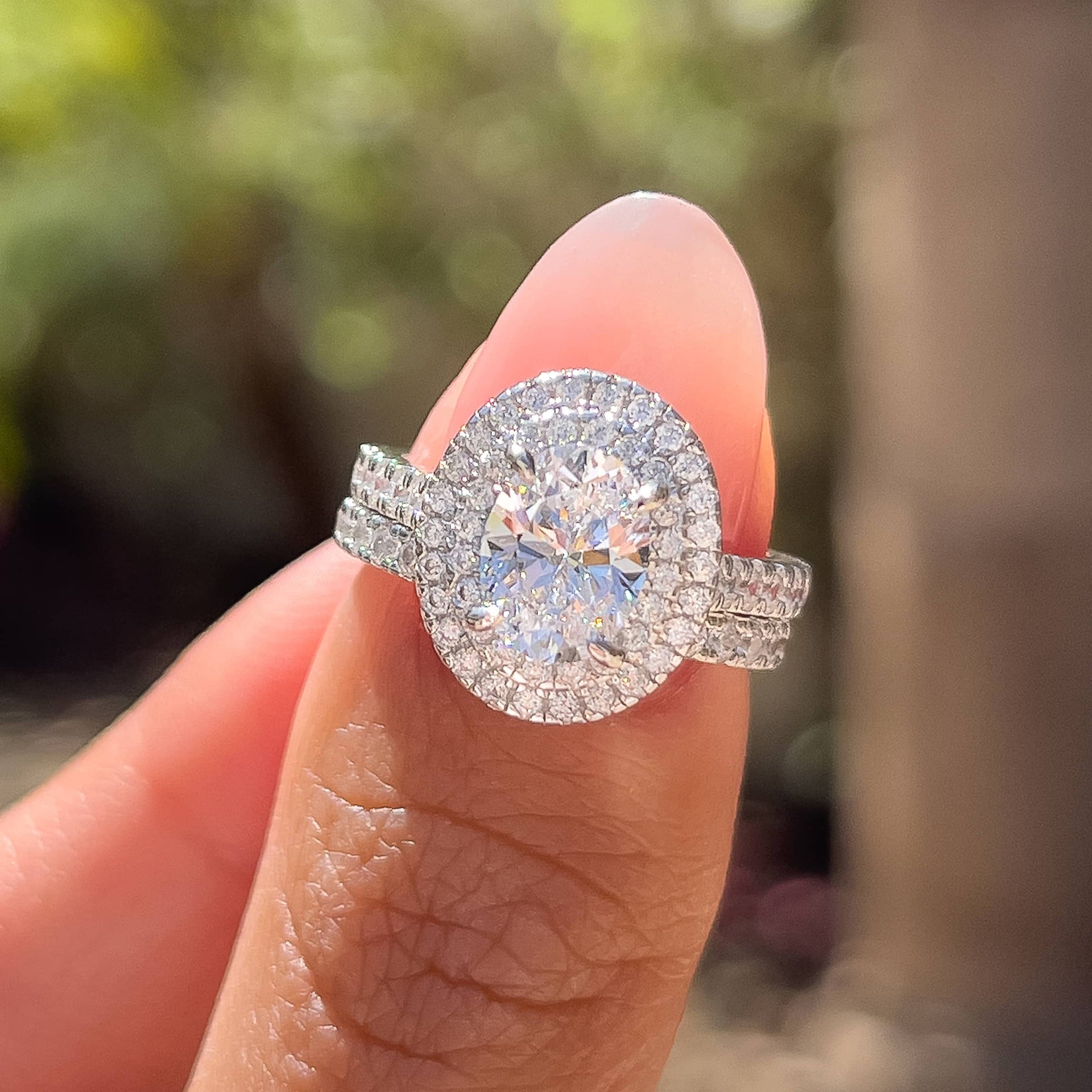 silver oval cut double halo engagement ring and matching half eternity wedding ring shown together by model with neutral pink nails