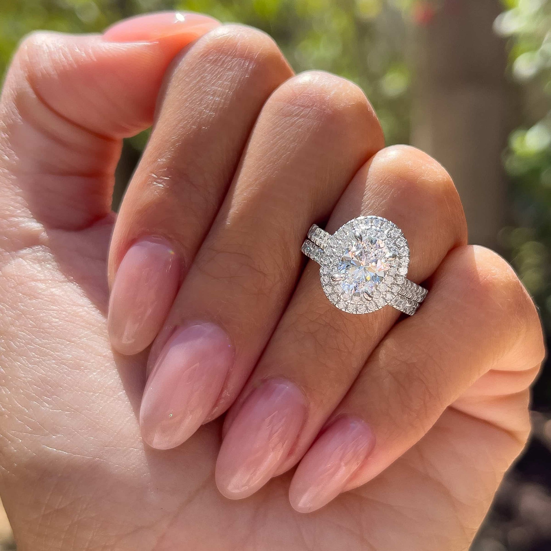 silver 1.5 carat oval cut wedding ring set worn by model with neutral colored nails