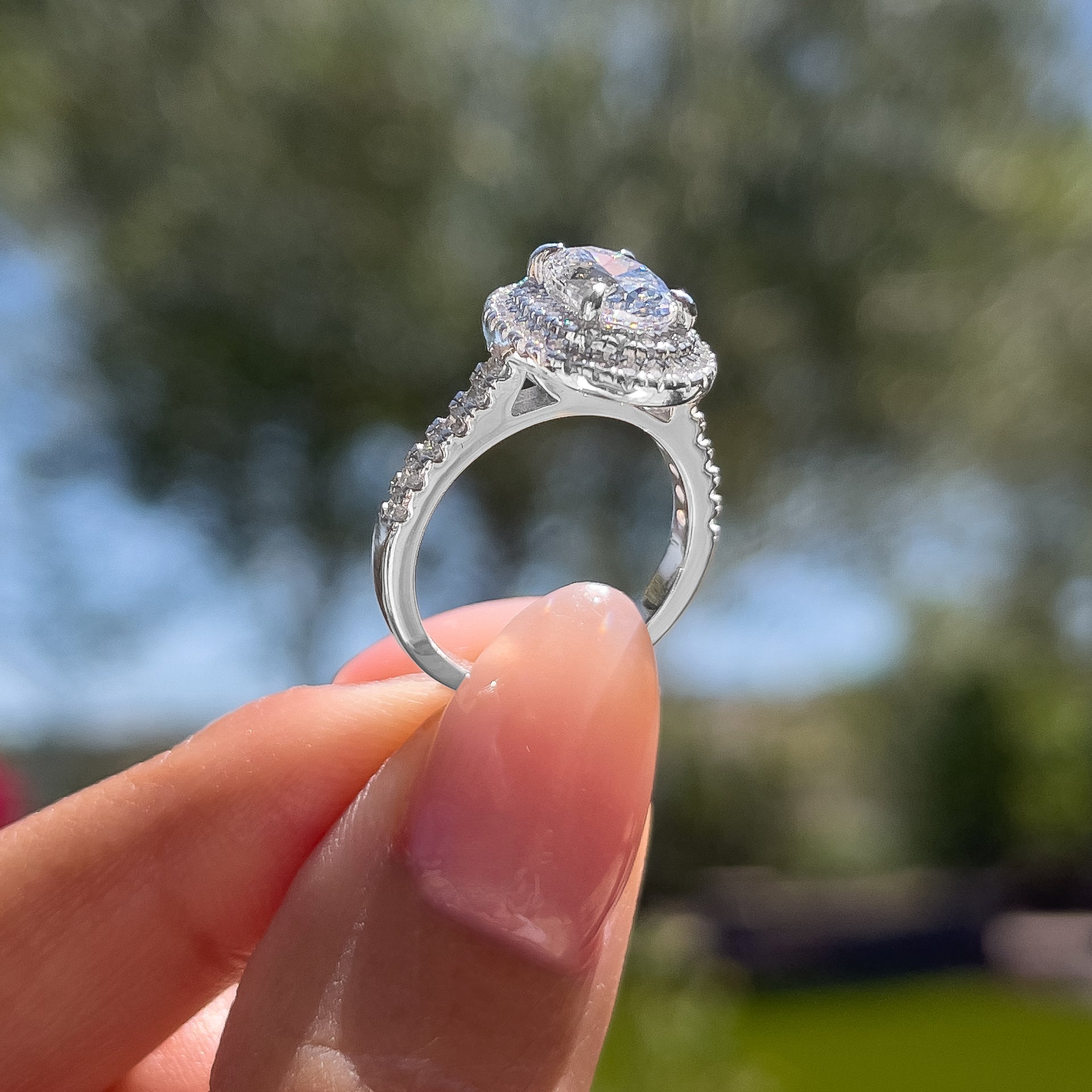 classic 1.5 carat oval cut double halo half eternity engagement ring shown at an alternate angle outdoors