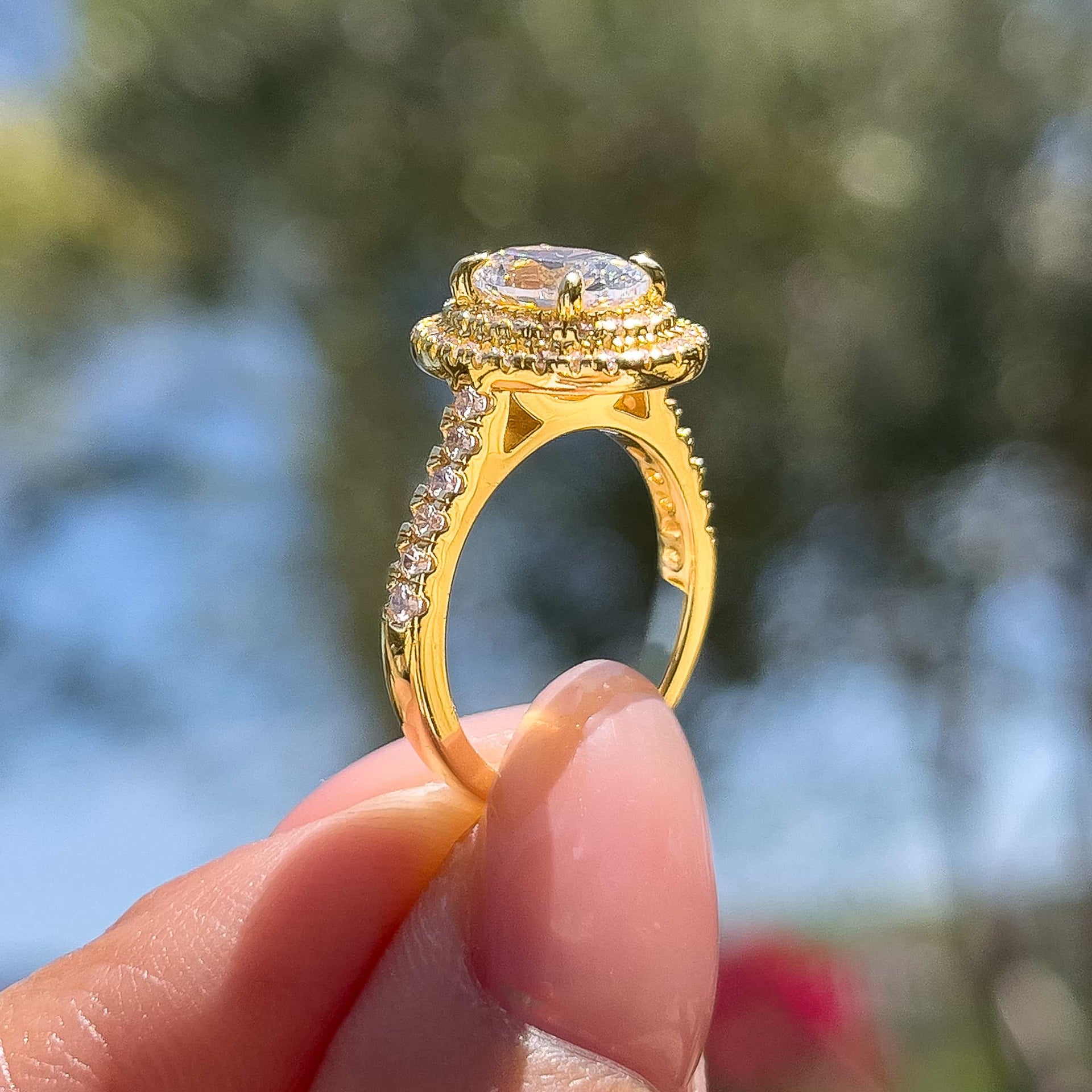 gold oval cut double halo engagement ring and matching half eternity wedding ring shown together by model with neutral pink nails