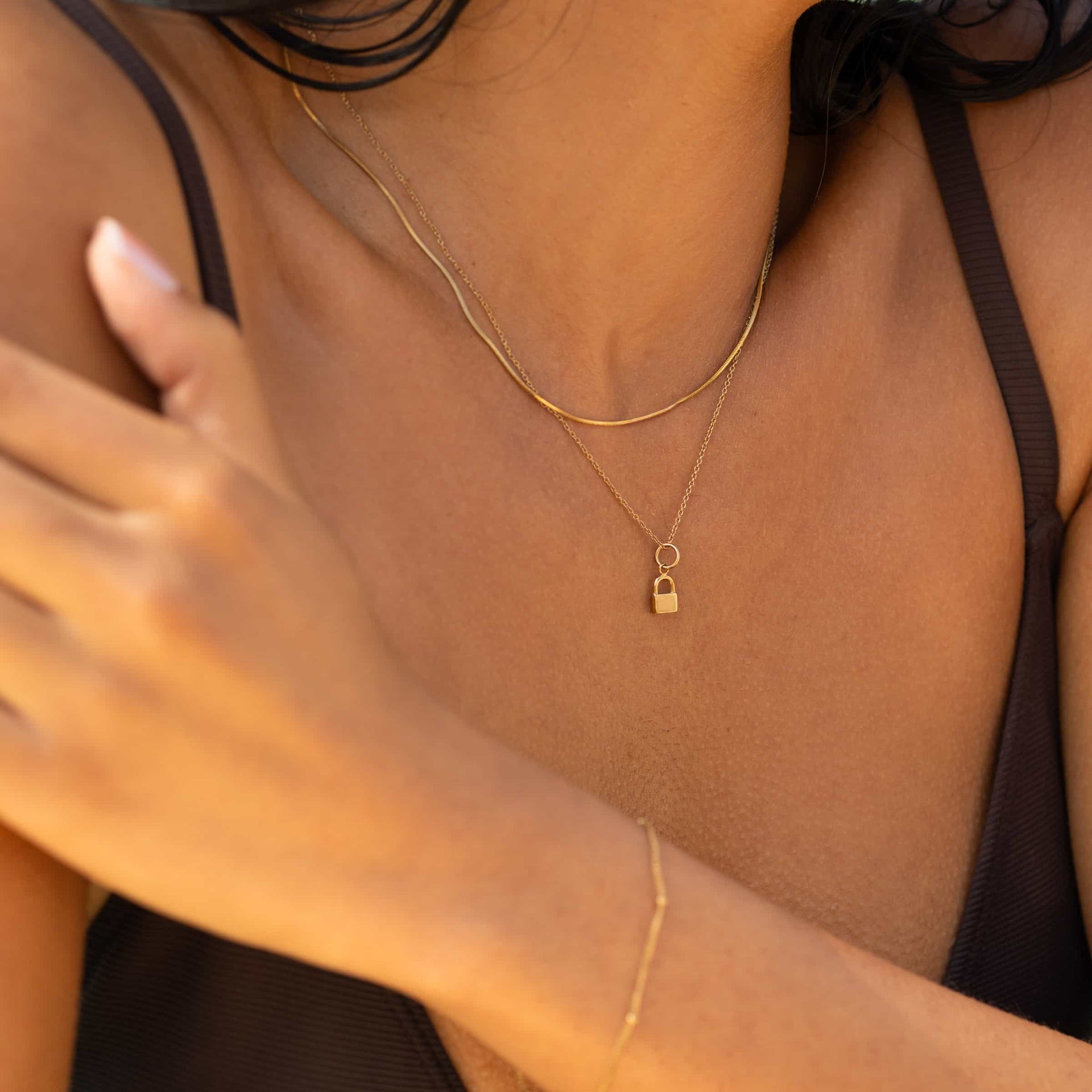Dainty Gold Cable Chain Necklace worn with a lock charm and layered snake chain necklace by model with dark hair