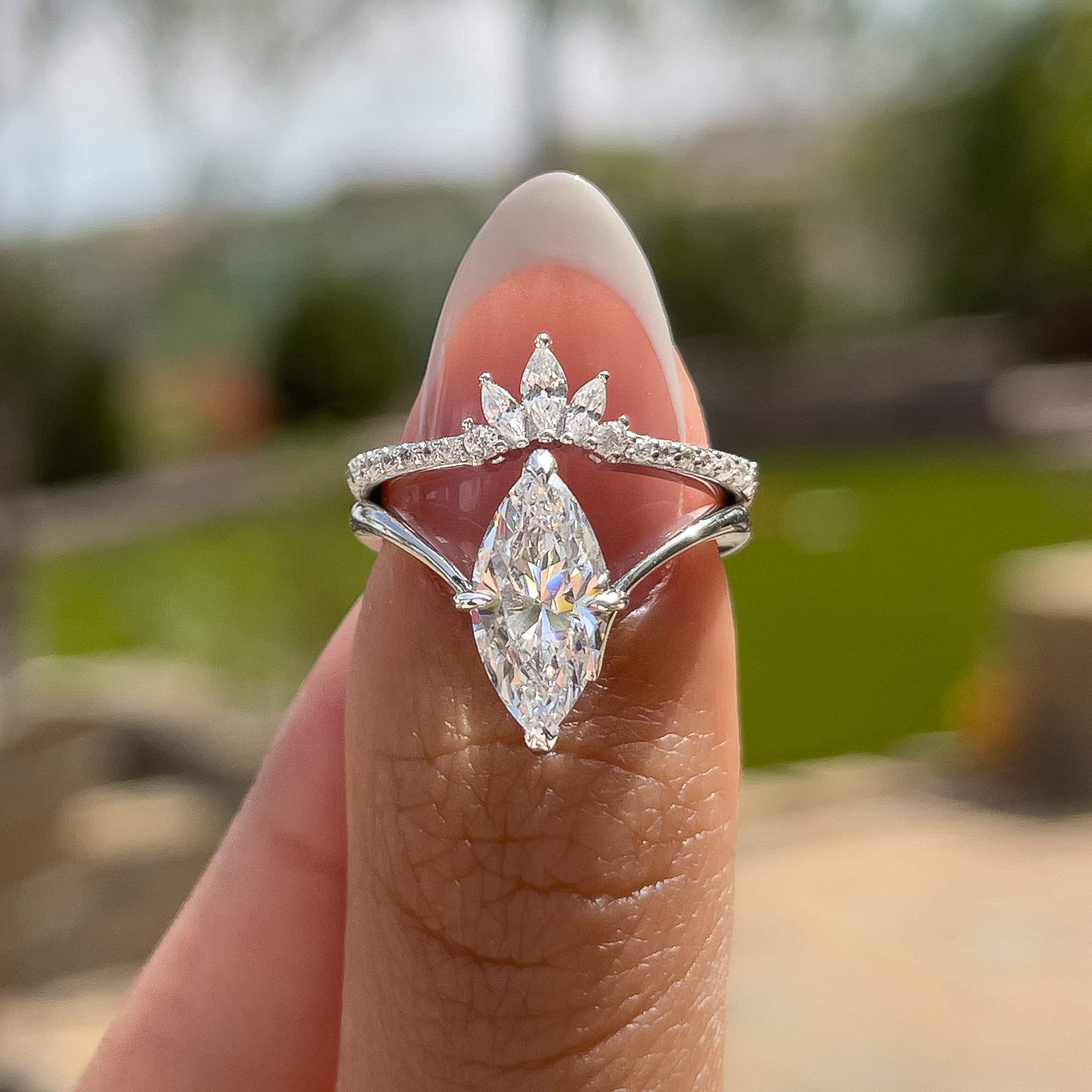 silver 2 carat marquise solitaire chevron engagement ring paired with a vintage wedding band held by a model with french tip nails