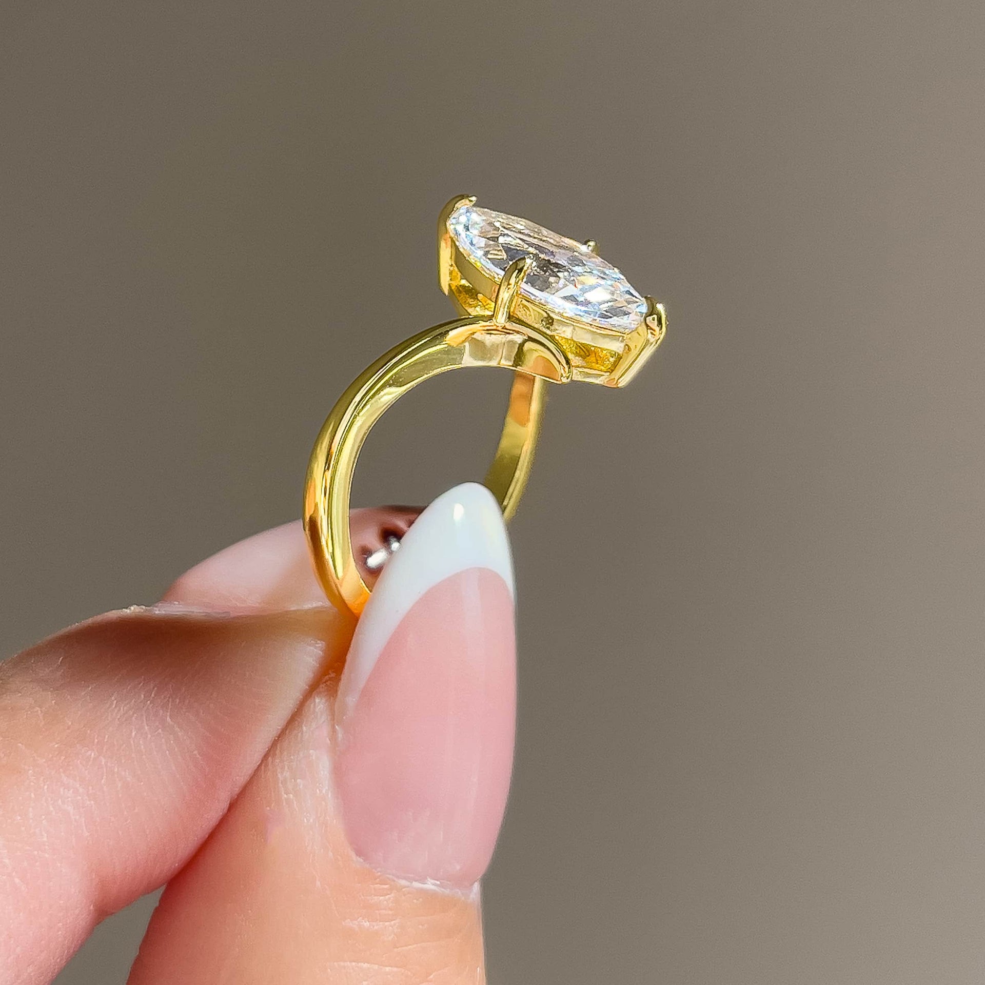 gold 2 carat marquise solitaire chevron engagement ring held by model with french tip nails