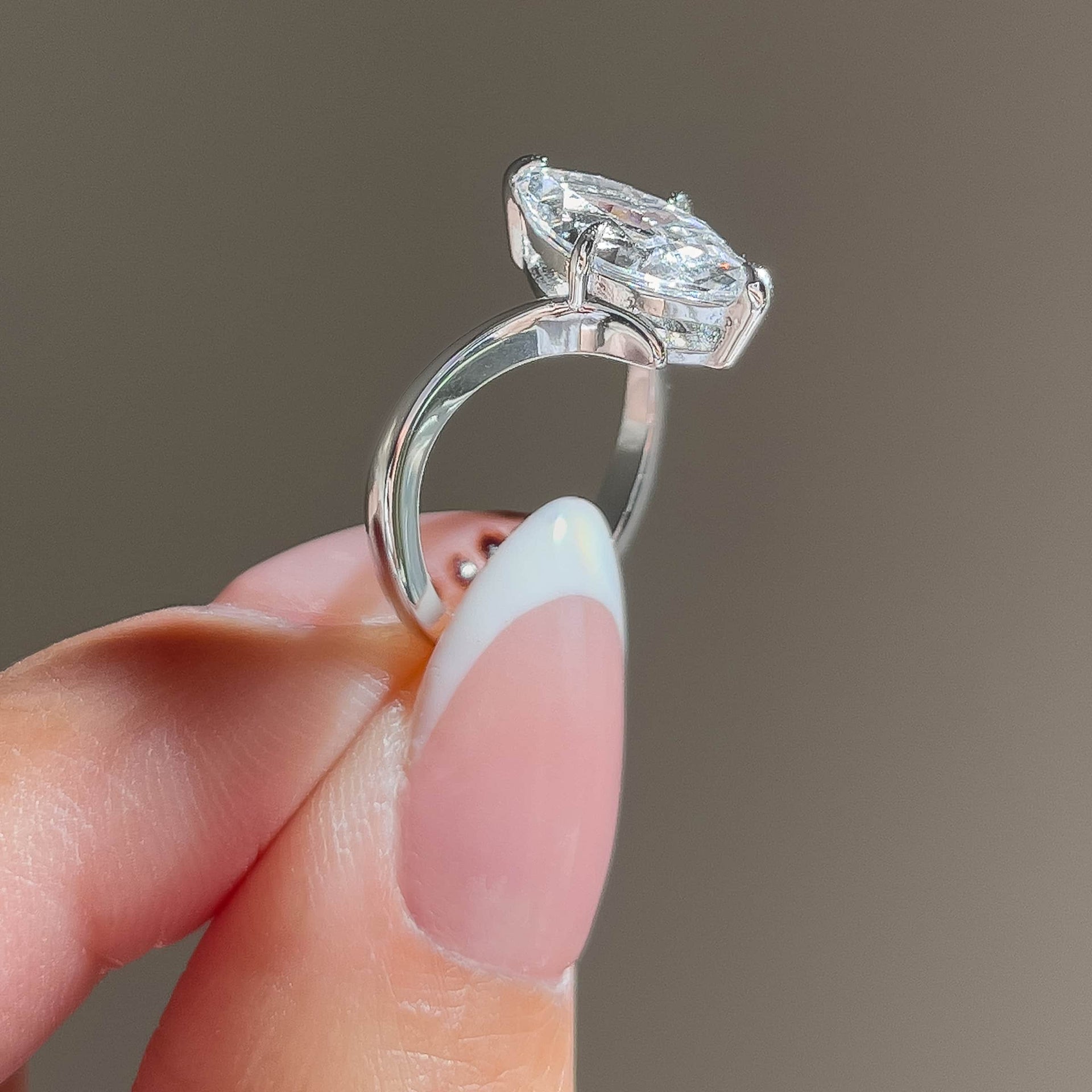 side view of a silver 2 carat marquise solitaire chevron engagement ring held by a model with french tip nails