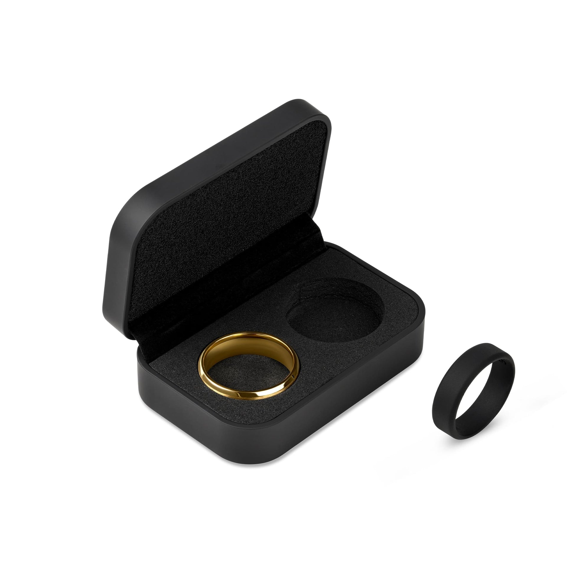 a black ring box opened to show the black padded exterior with a gold band inserted into one of the slots and a black silicone ring positioned to the side on a white background