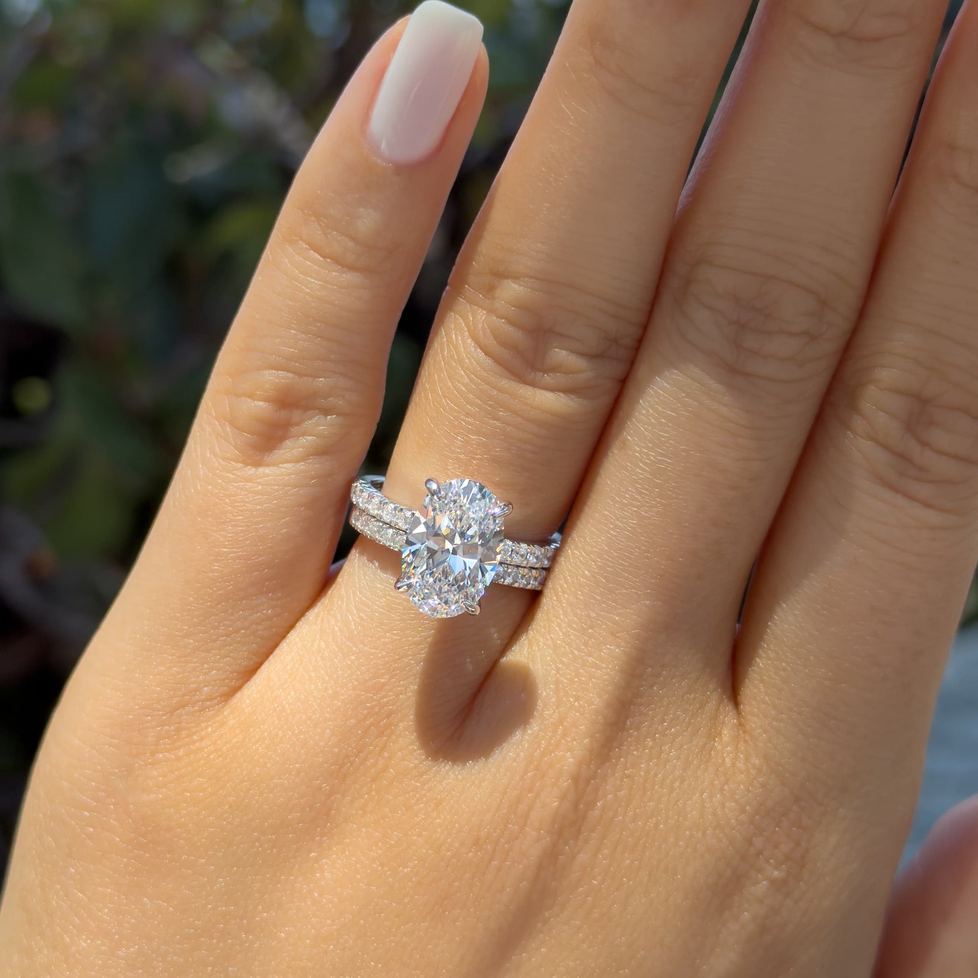 silver 4 carat oval cut half eternity engagement ring paired with a matching wedding band worn by mode with short, white nails
