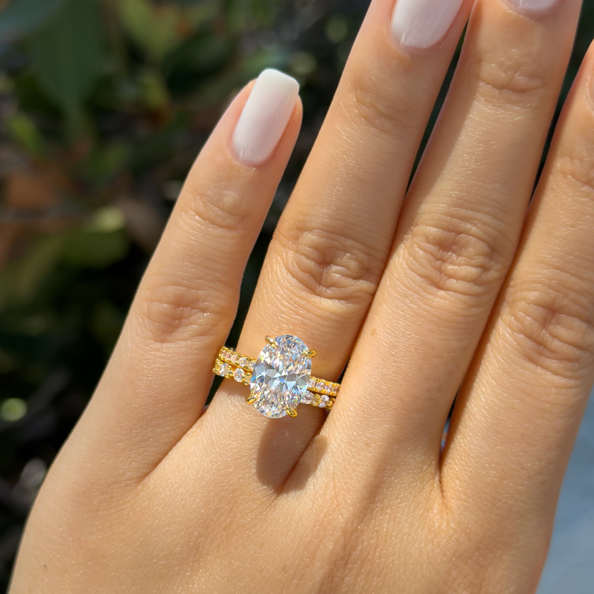 gold 4 carat oval cut half eternity engagement ring paired with a vintage style wedding band worn by mode with short, white nails