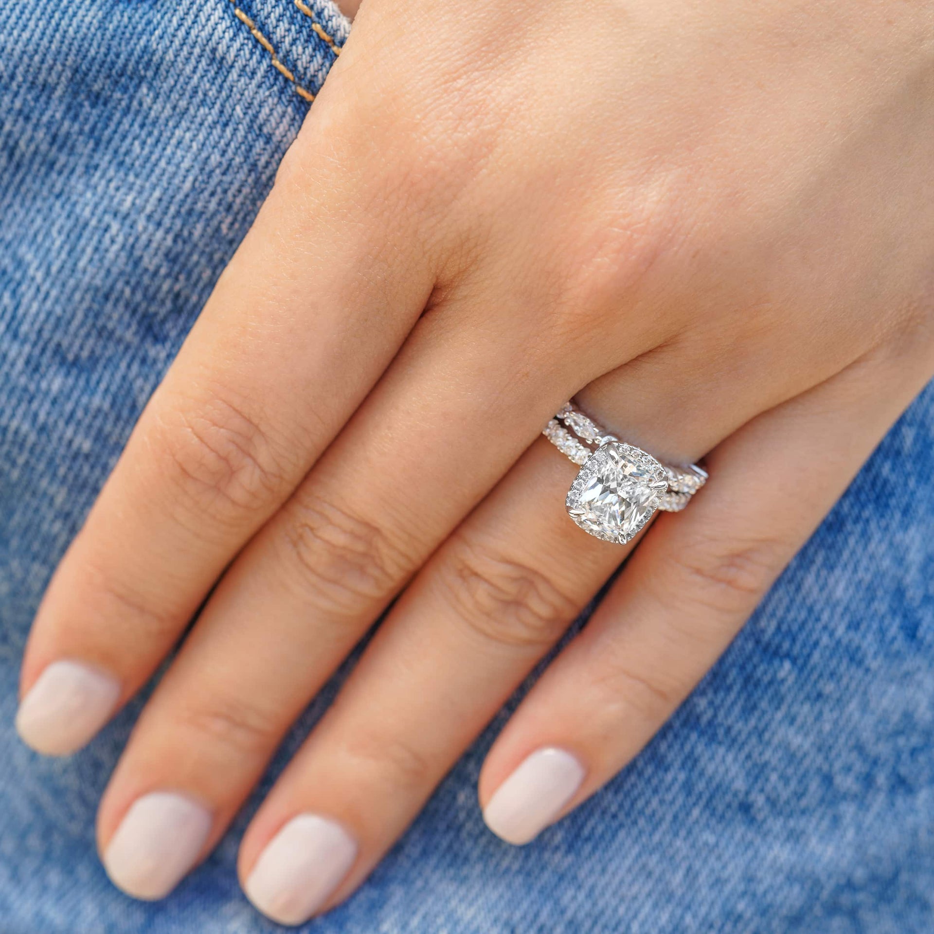 silver 3 carat elongated cushion cut halo engagement ring paired with unique wedding band worn by model wearing denim