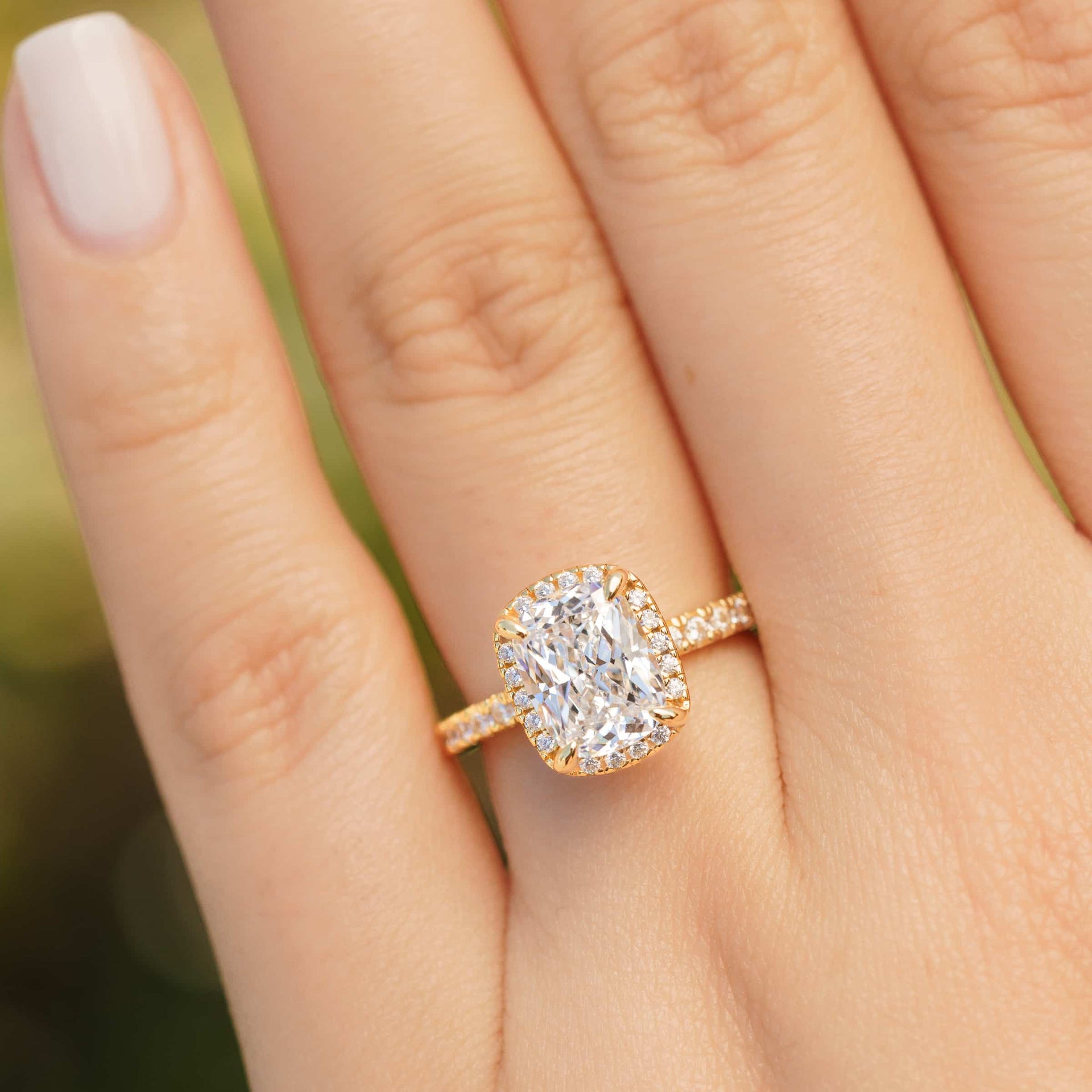 gold 3 carat elongated cushion cut halo engagement ring worn by model with neutral nails
