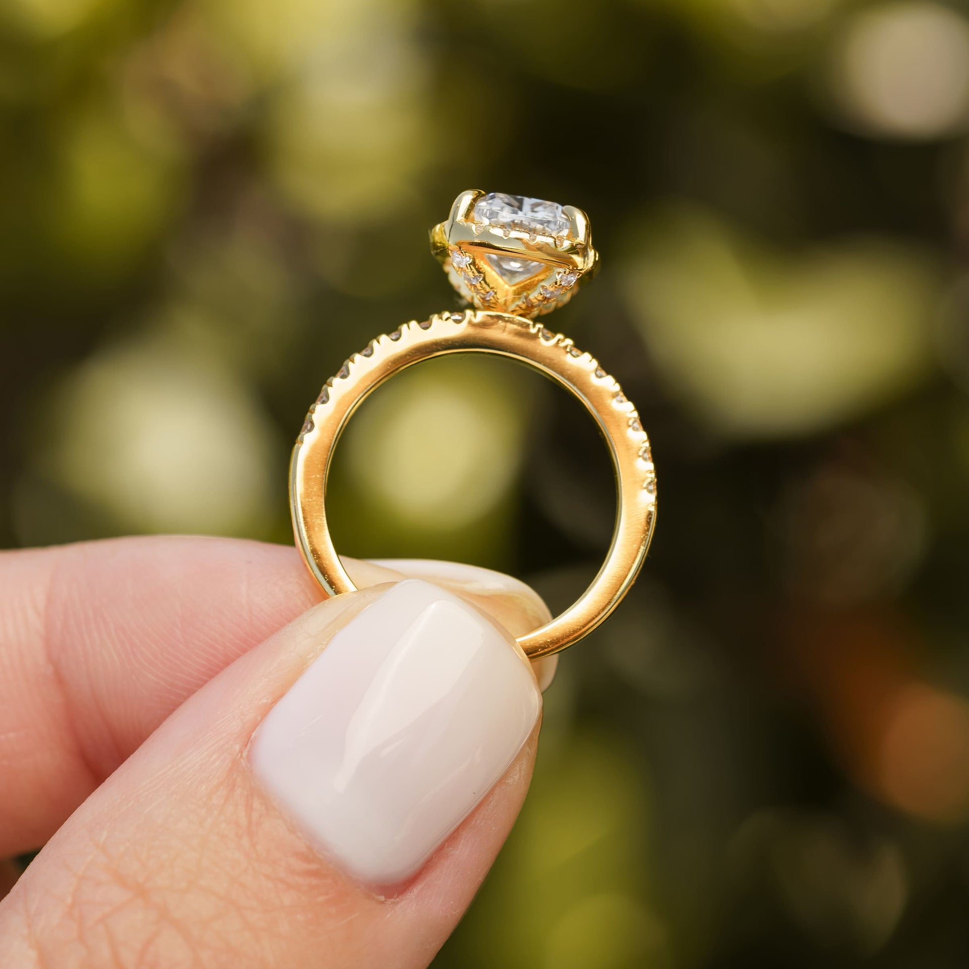 side view of gold 3 carat elongated cushion cut halo engagement ring held by model with neutral nails