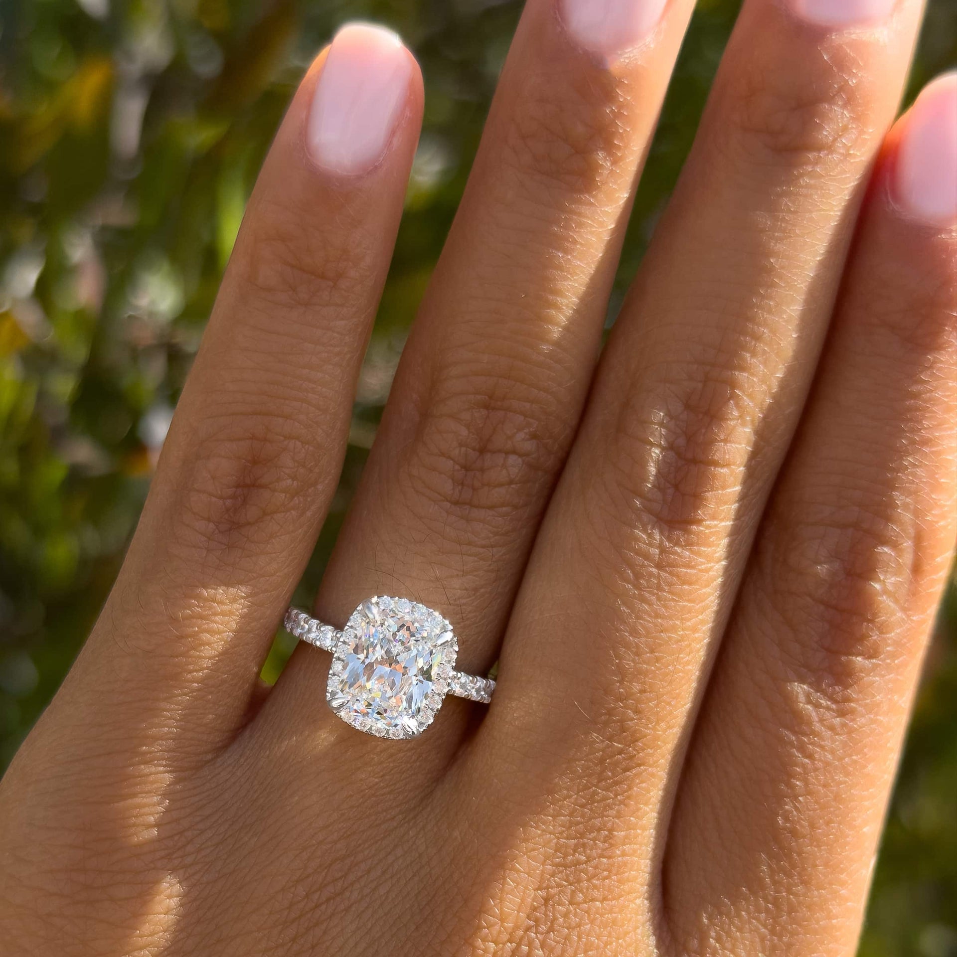 silver 3 carat elongated cushion cut halo engagement ring worn by model with light pink nails