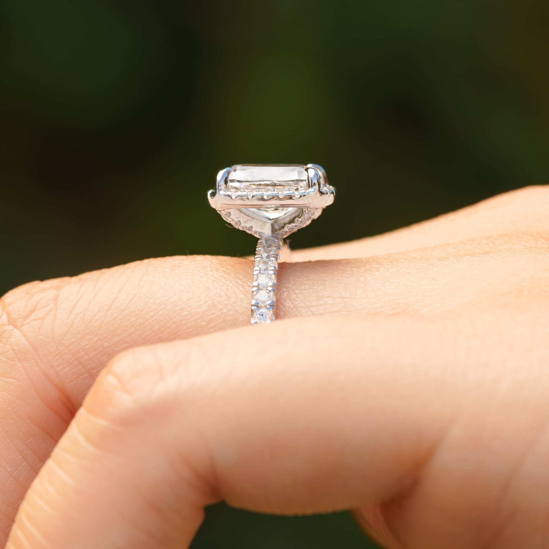 side view of silver 3 carat elongated cushion cut halo engagement ring worn by model