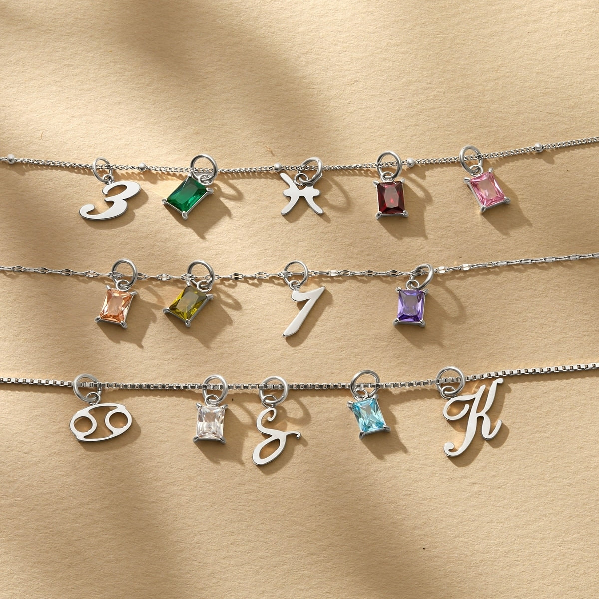 a stunning flatlay of a variety of stainless steel charms, all modeled on various chain necklaces atop a tan and textured background