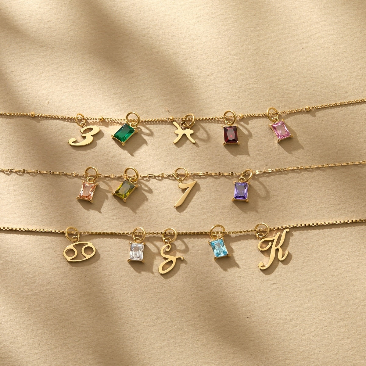 a stunning flatlay of a variety of 14k Gold PVD plated stainless steel charms, all modeled on various chain necklaces atop a tan and textured background