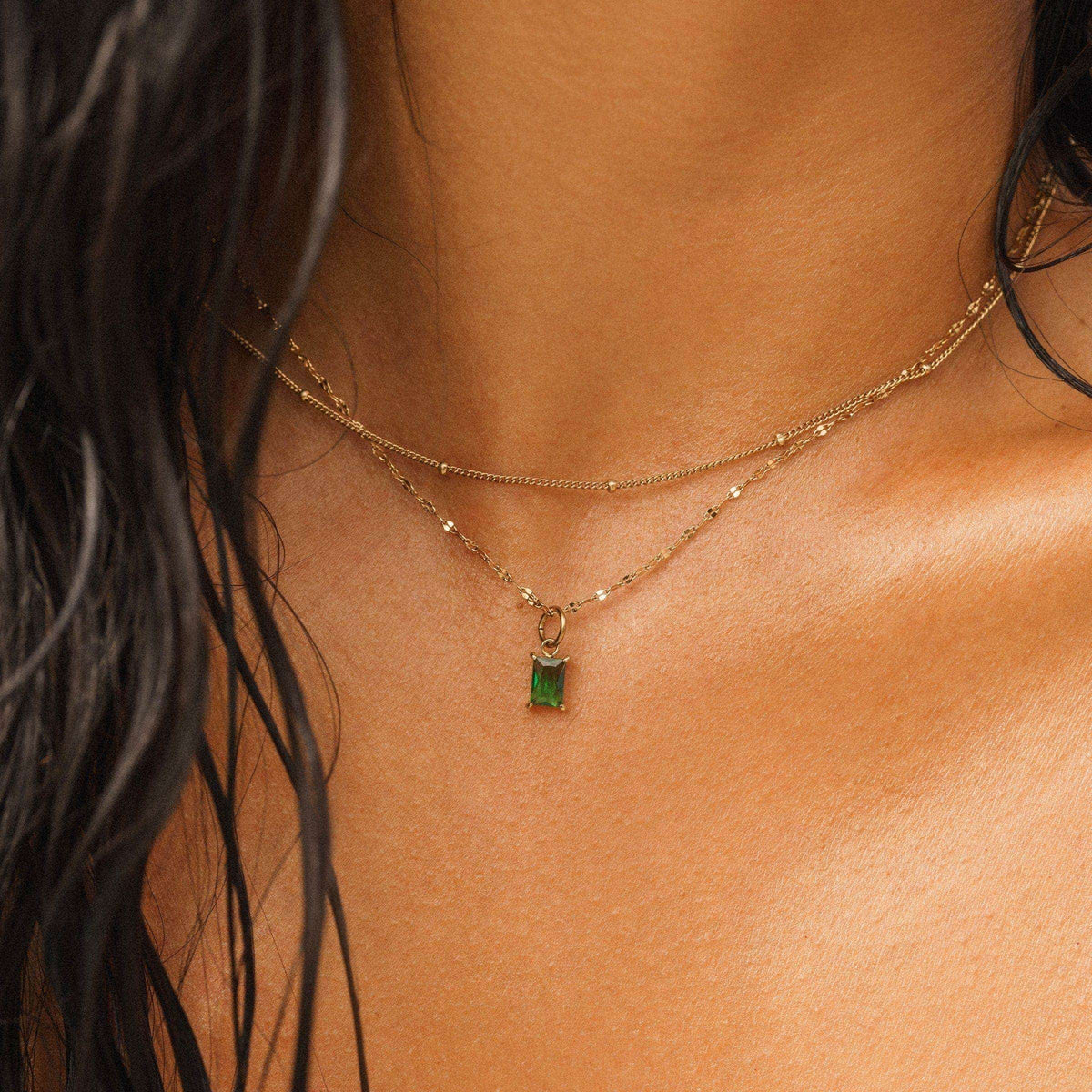 a simple 14k gold pvd plated stainless steel satellite chain necklace worn layered with another stainless steel necklace and a birthstone charm on a model 