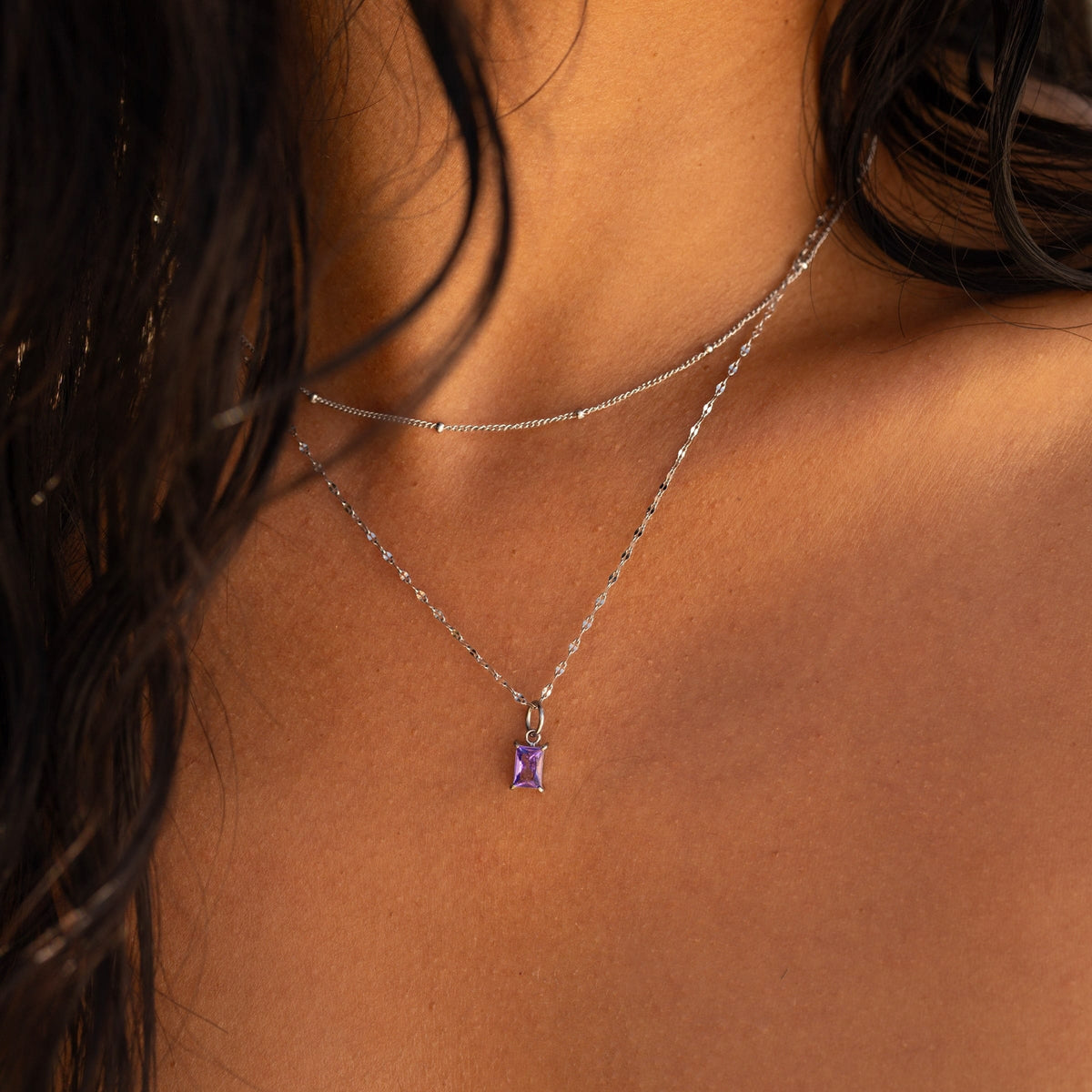 a simple stainless steel satellite chain necklace worn layered with another stainless steel necklace on a model 