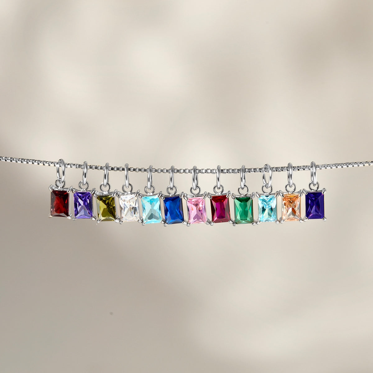 all 12 available radiant cut birthstone charms shown dangling on a silver box chain
