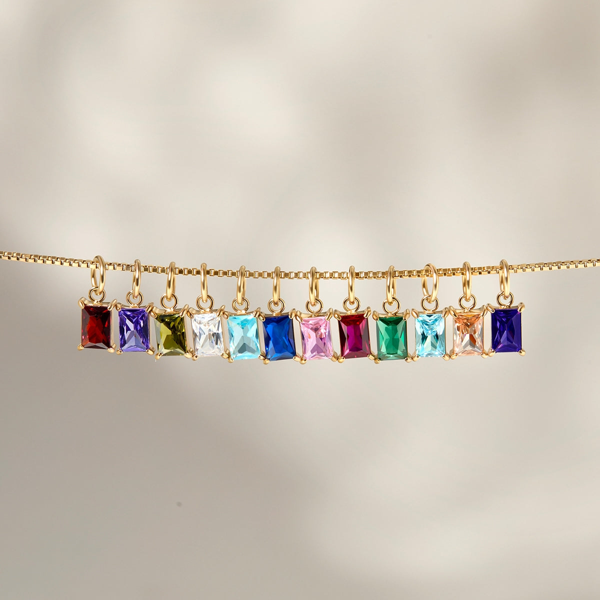 all 12 available radiant cut birthstone charms shown dangling on a gold box chain