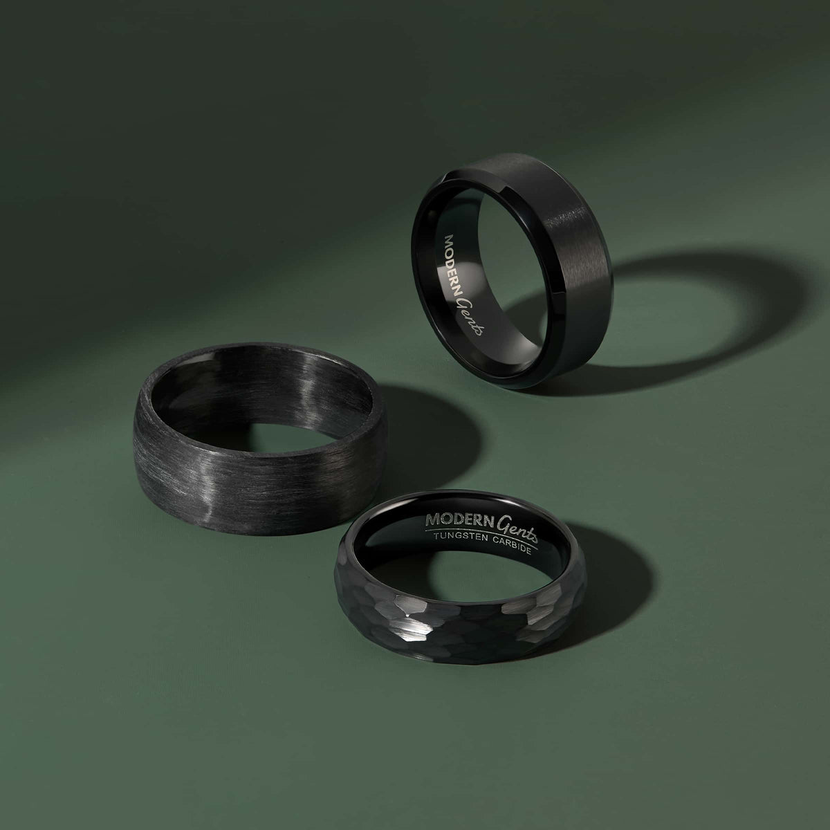 three various stainless steel, tungsten carbide, and carbon fiber bands on a dark green background