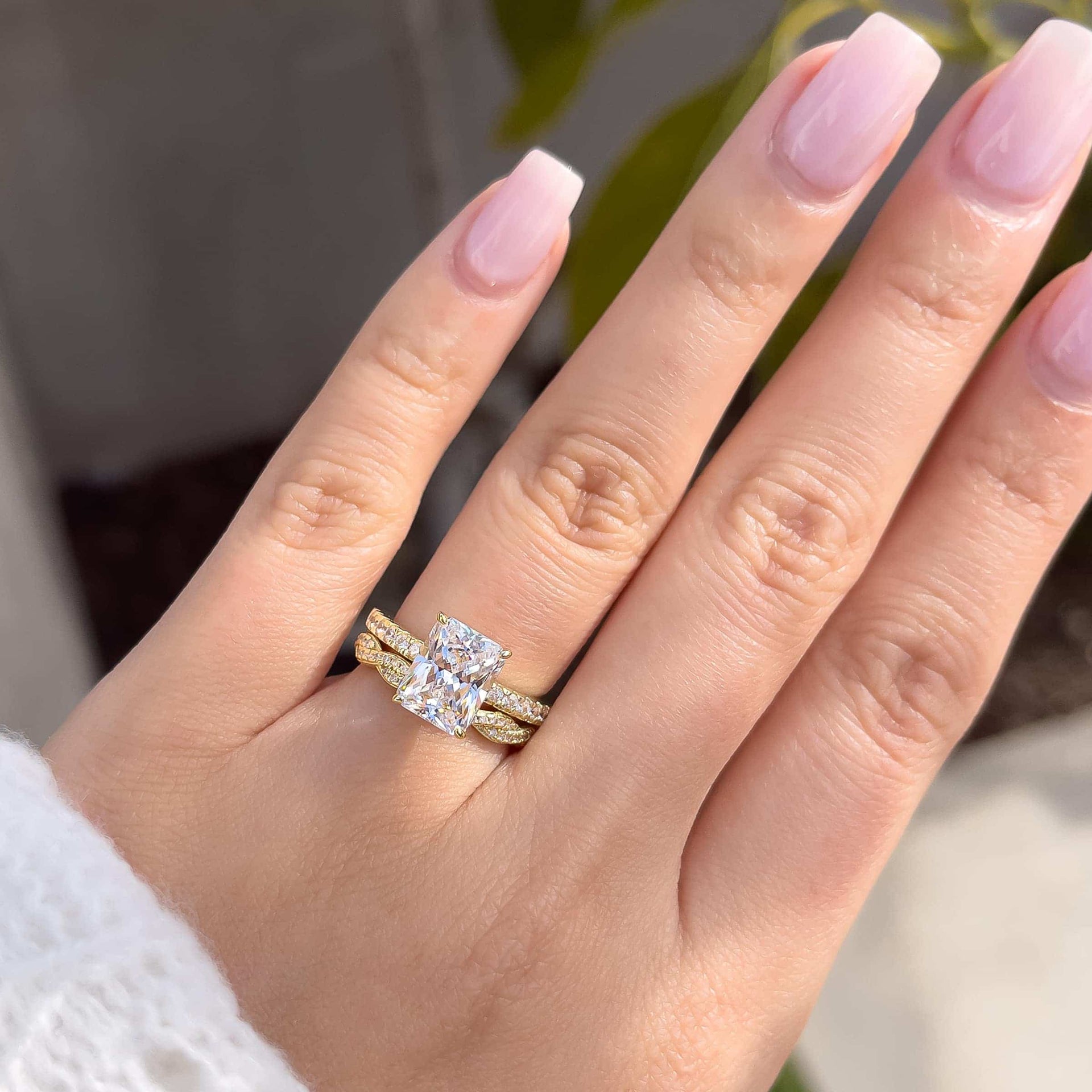 3 carat engagement ring shown in gold paired with a vintage twisting detail band shown on model with light pink nails and white sweater