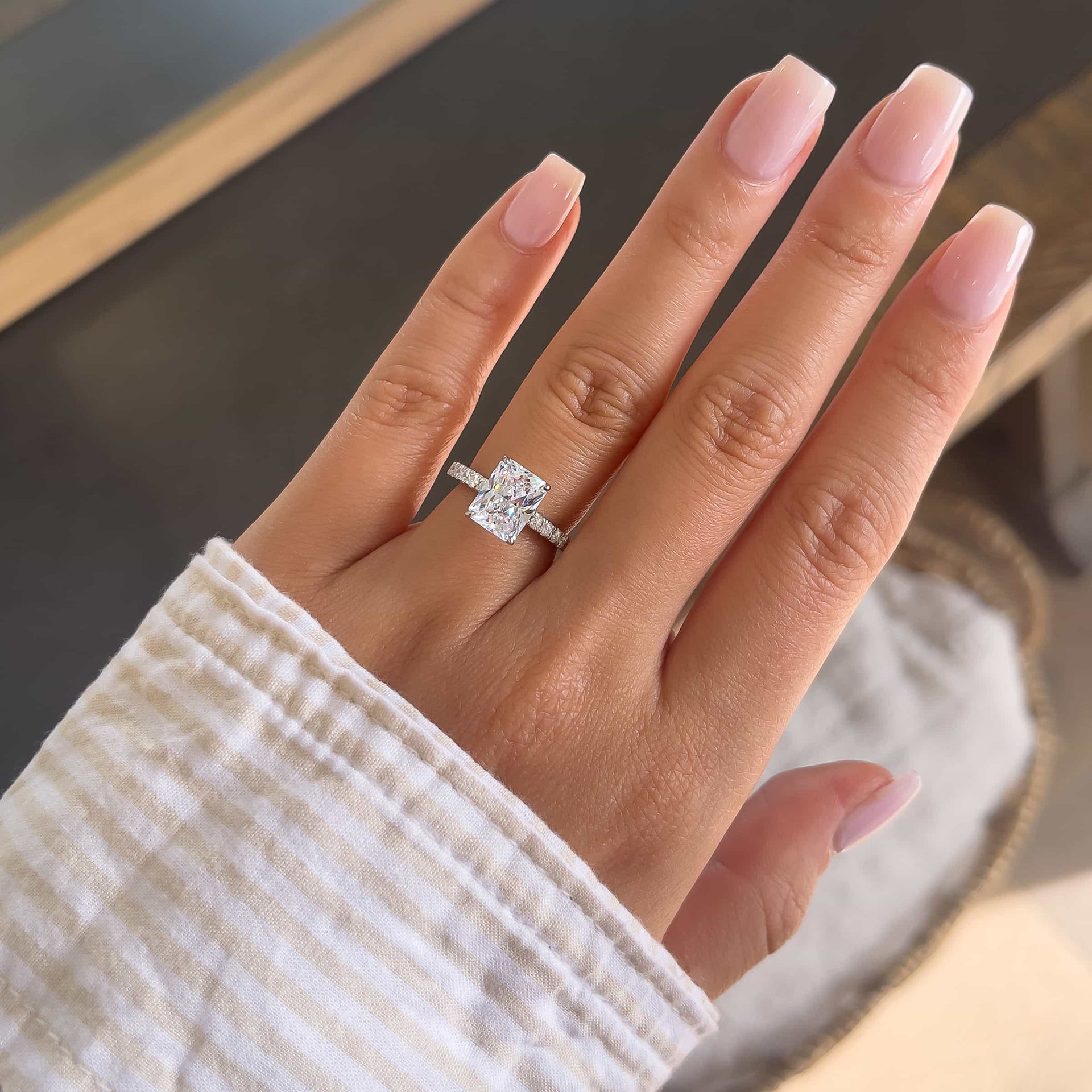 Radiant cut engagement ring with dazzling half eternity band detailing modeled on female hand with light pink nails and striped shirt