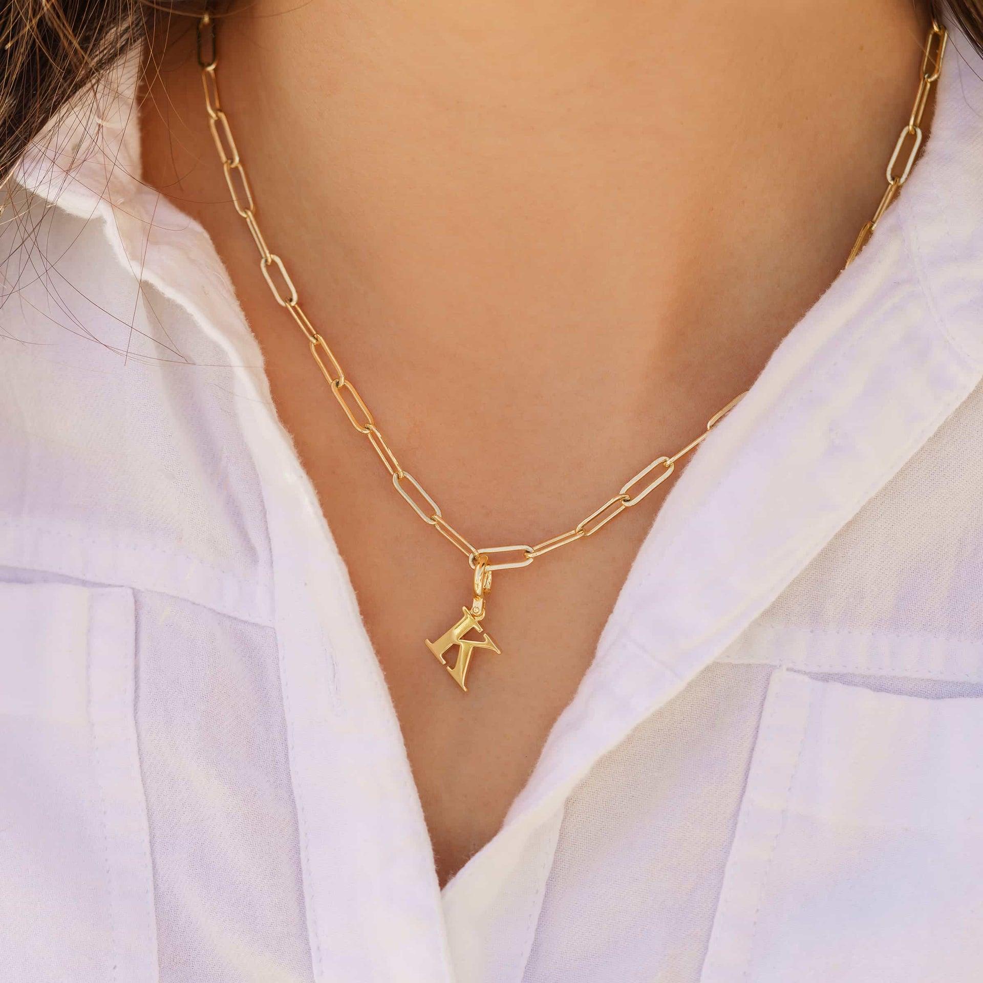 gold letter charm shown in "K" on gold necklace worn by model with white top