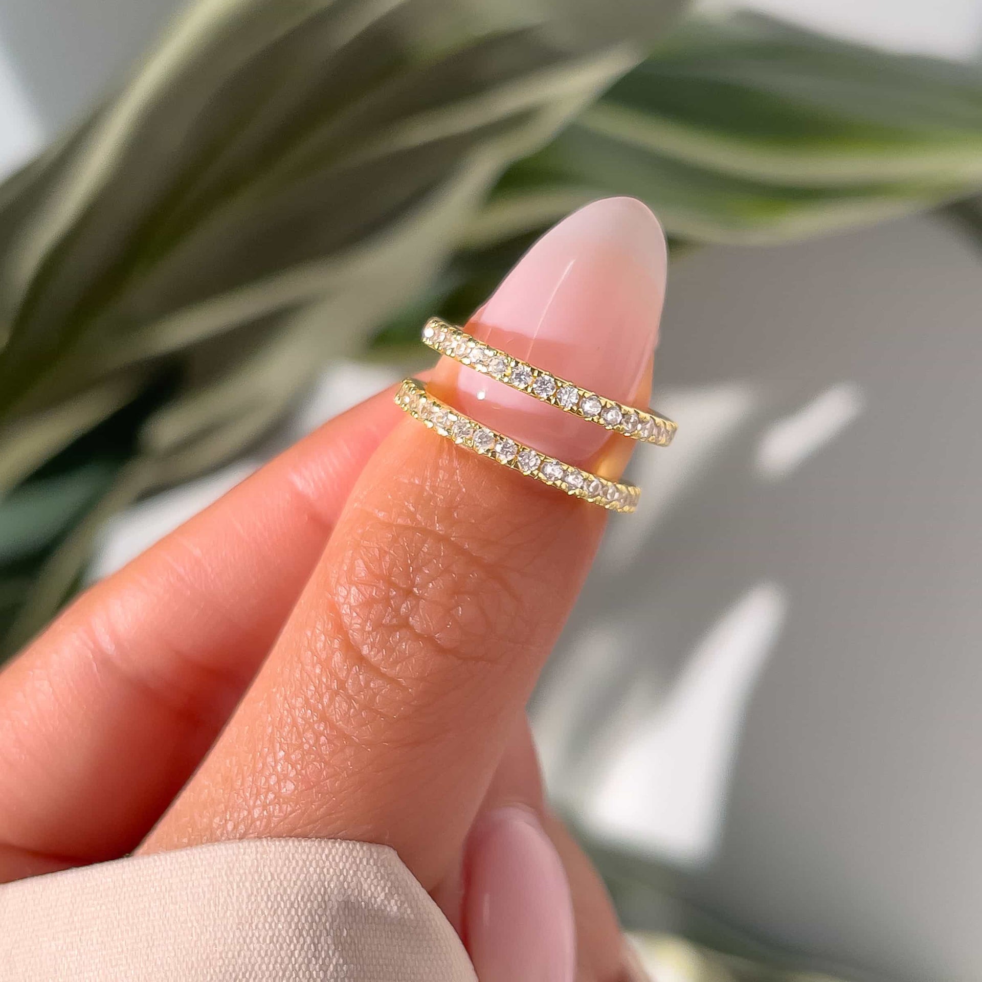 woman pinching two gold desire wedding bands with greenery in background