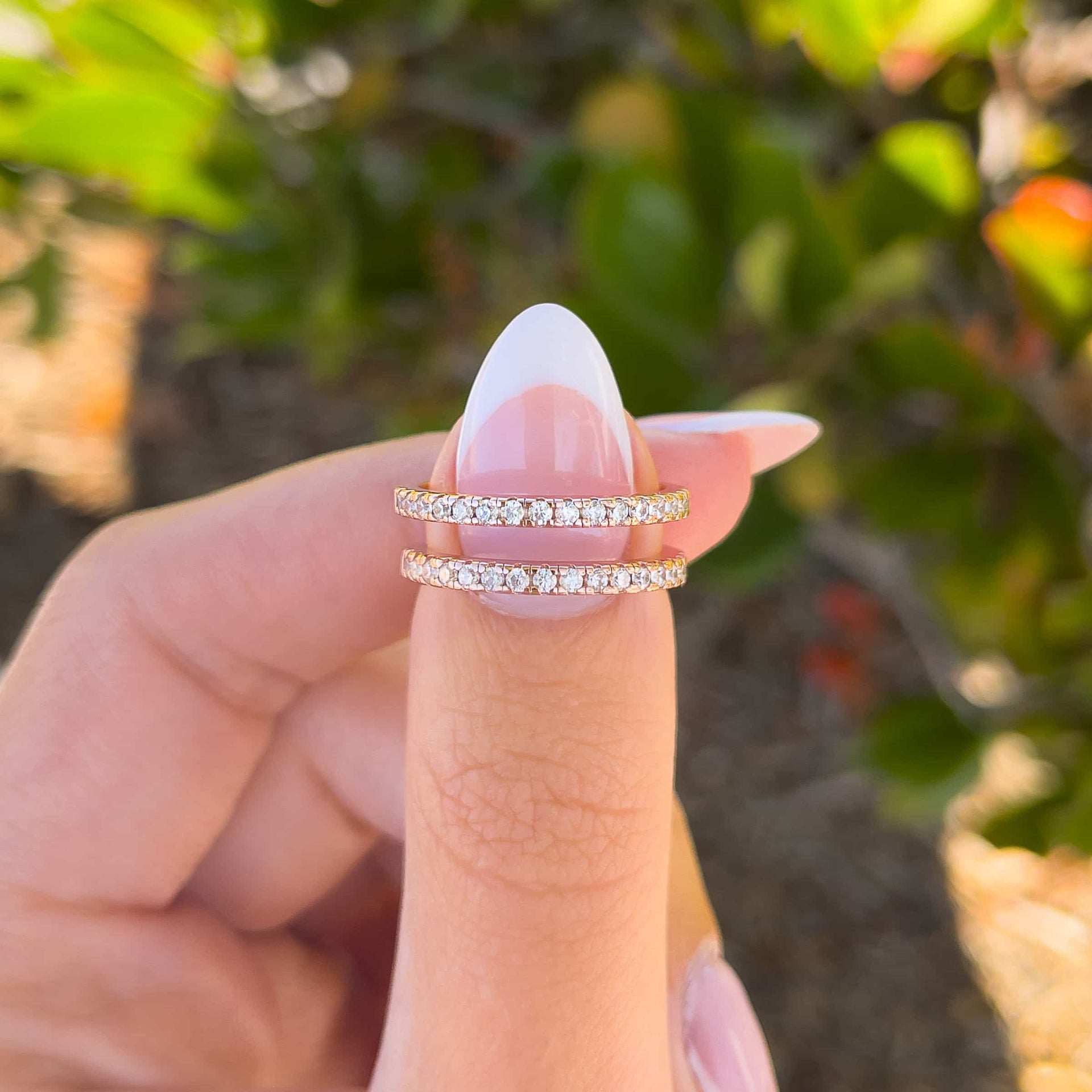 woman pinching two rose gold half eternity wedding bands with greenery in background