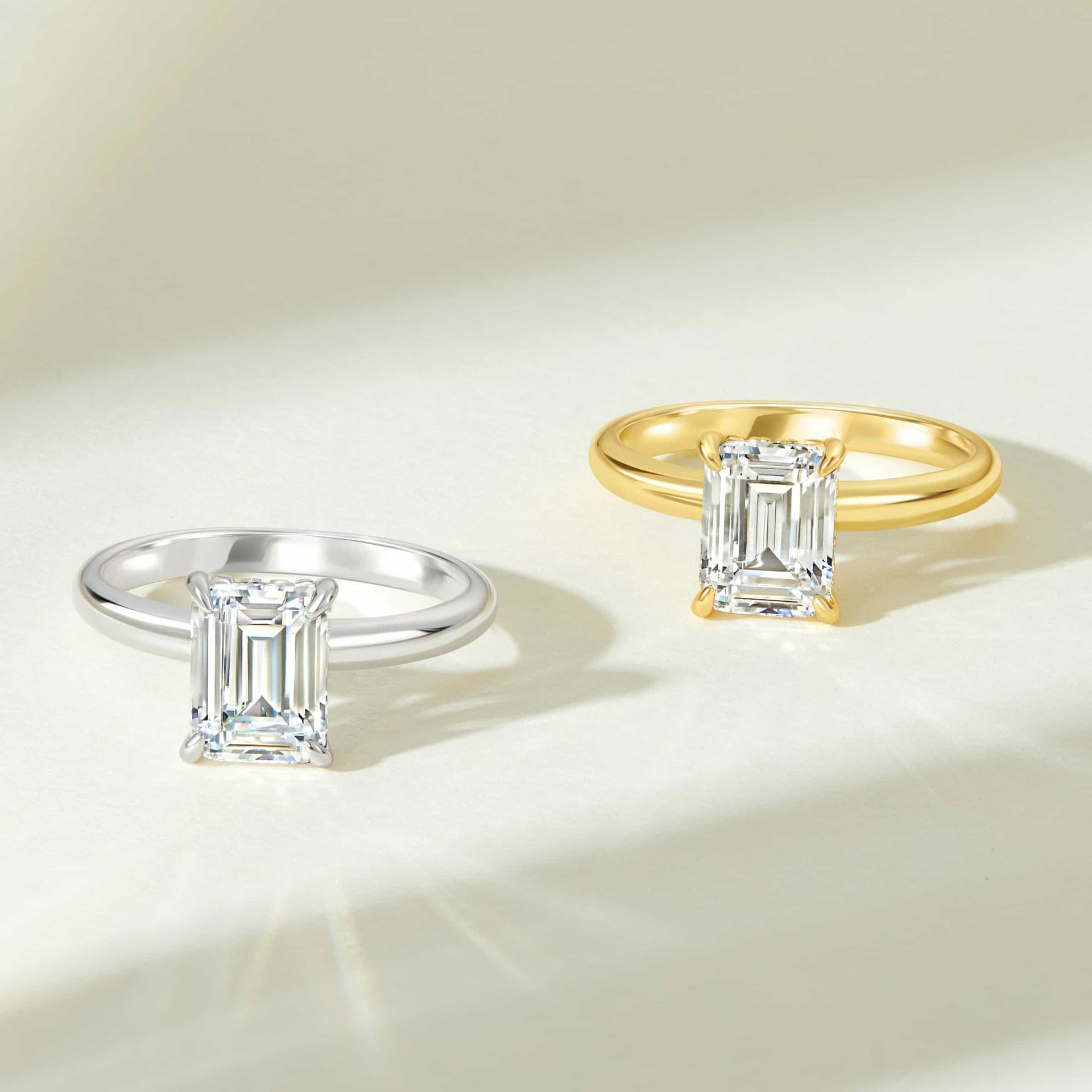 stunning emerald cut solitaire engagement rings shown in silver and gold on light white cream background