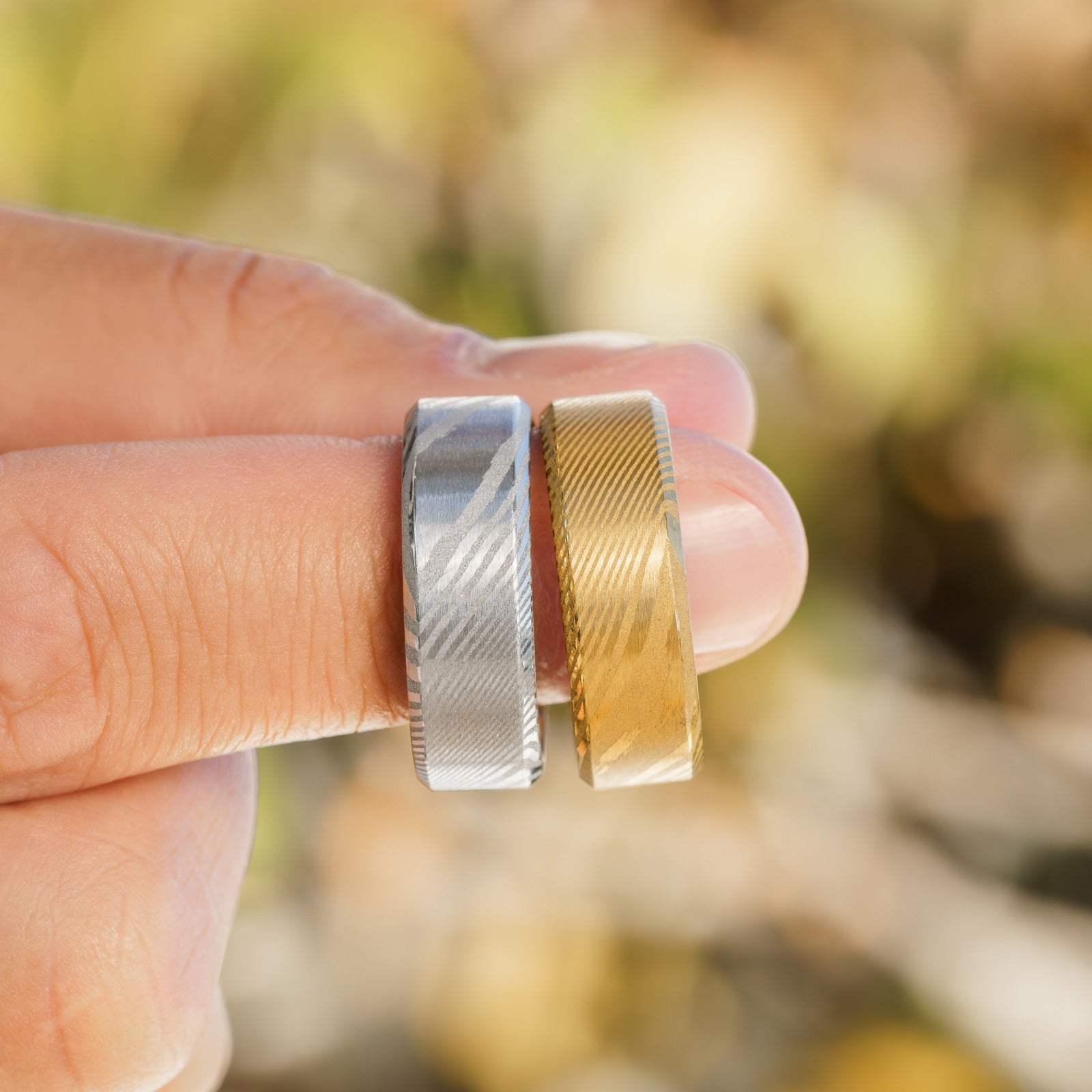 One silver and one gold Damascus steel men's wedding ring modeled on a finger