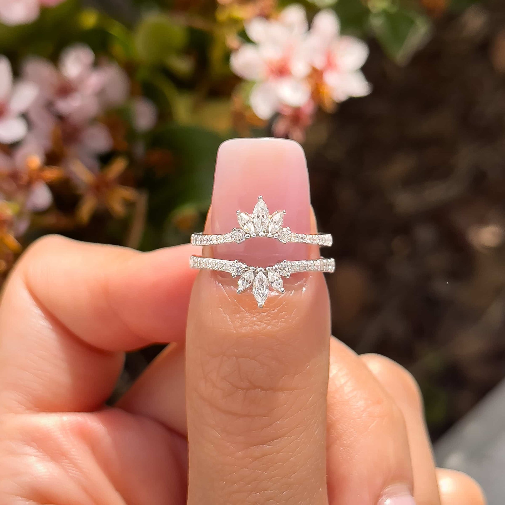 woman pinching two silver wedding bands with flowers in background