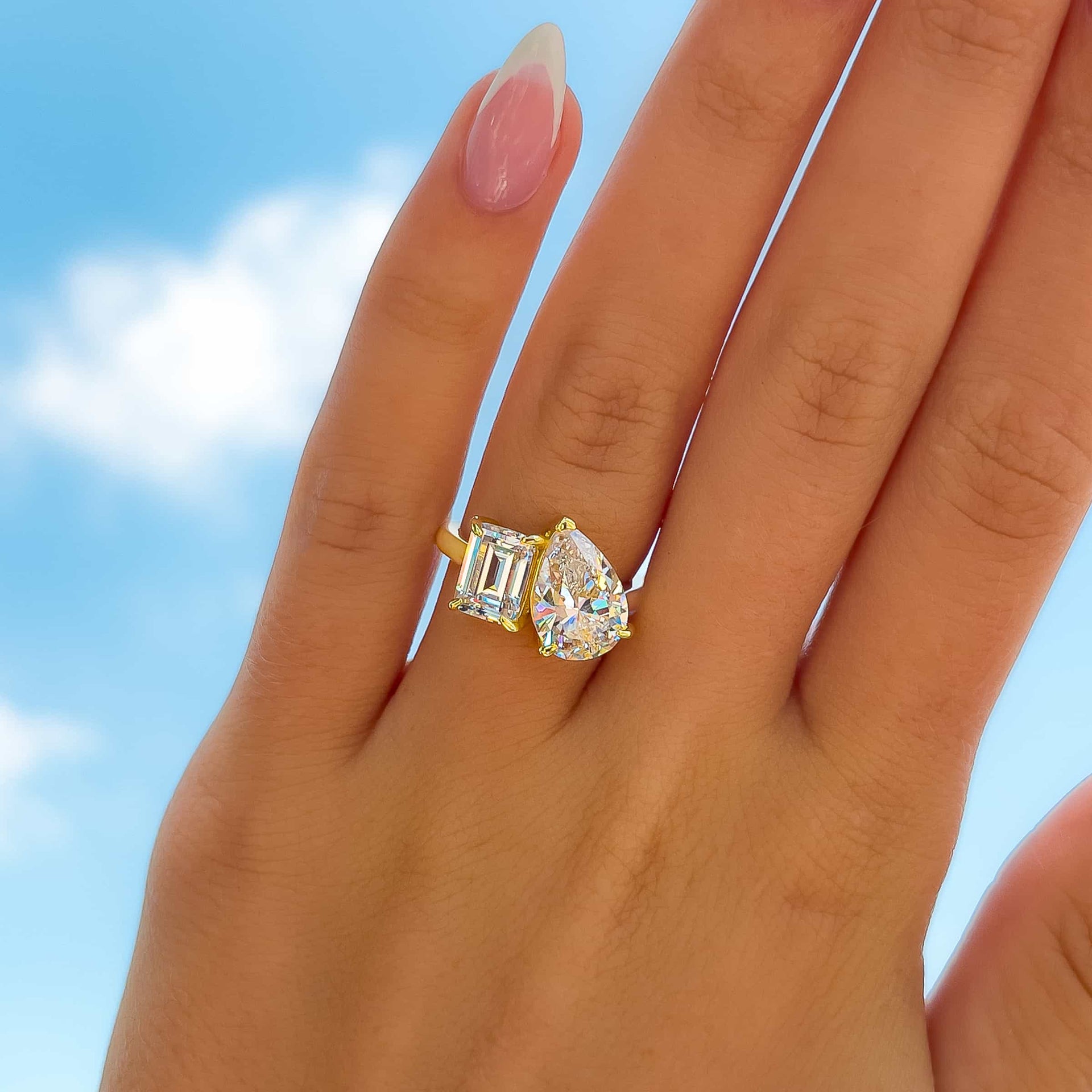 gold modern toi et moi pear and emerald cut engagement ring on model with almond shaped french tip nails