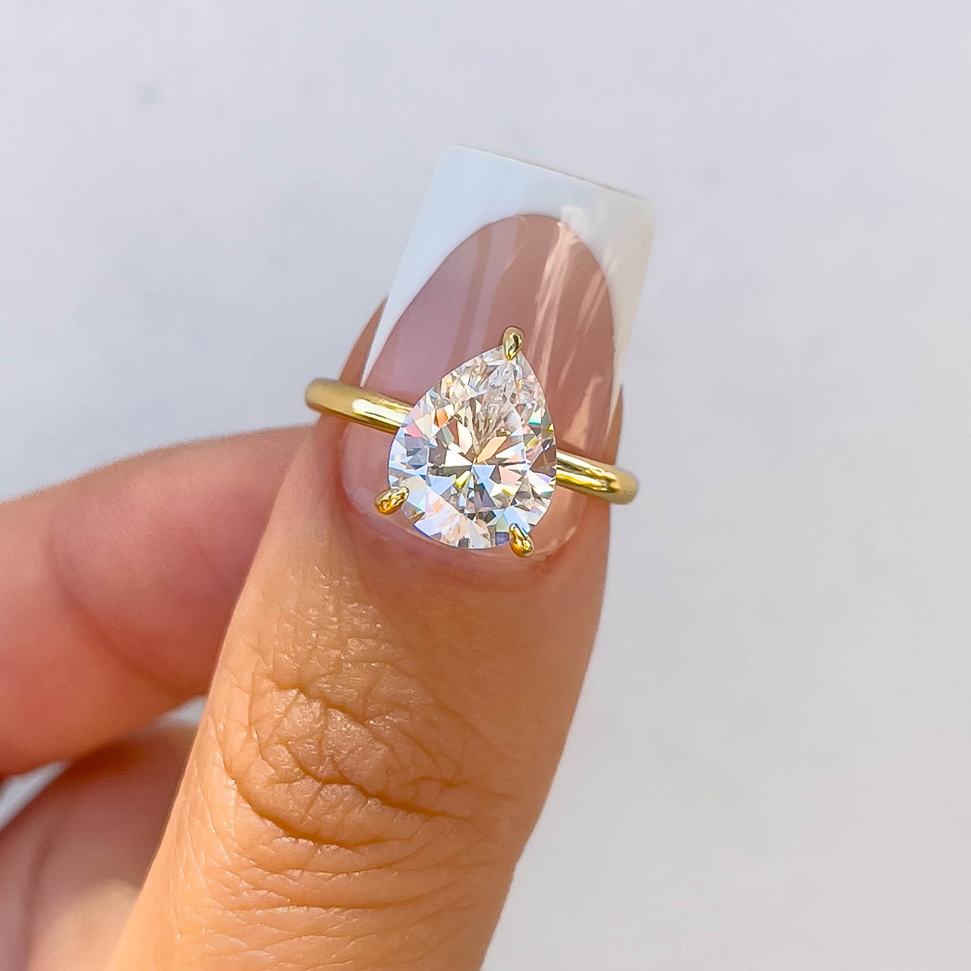 stunning 3 carat pear cut solitaire ring with a hidden halo on model with french tip nails