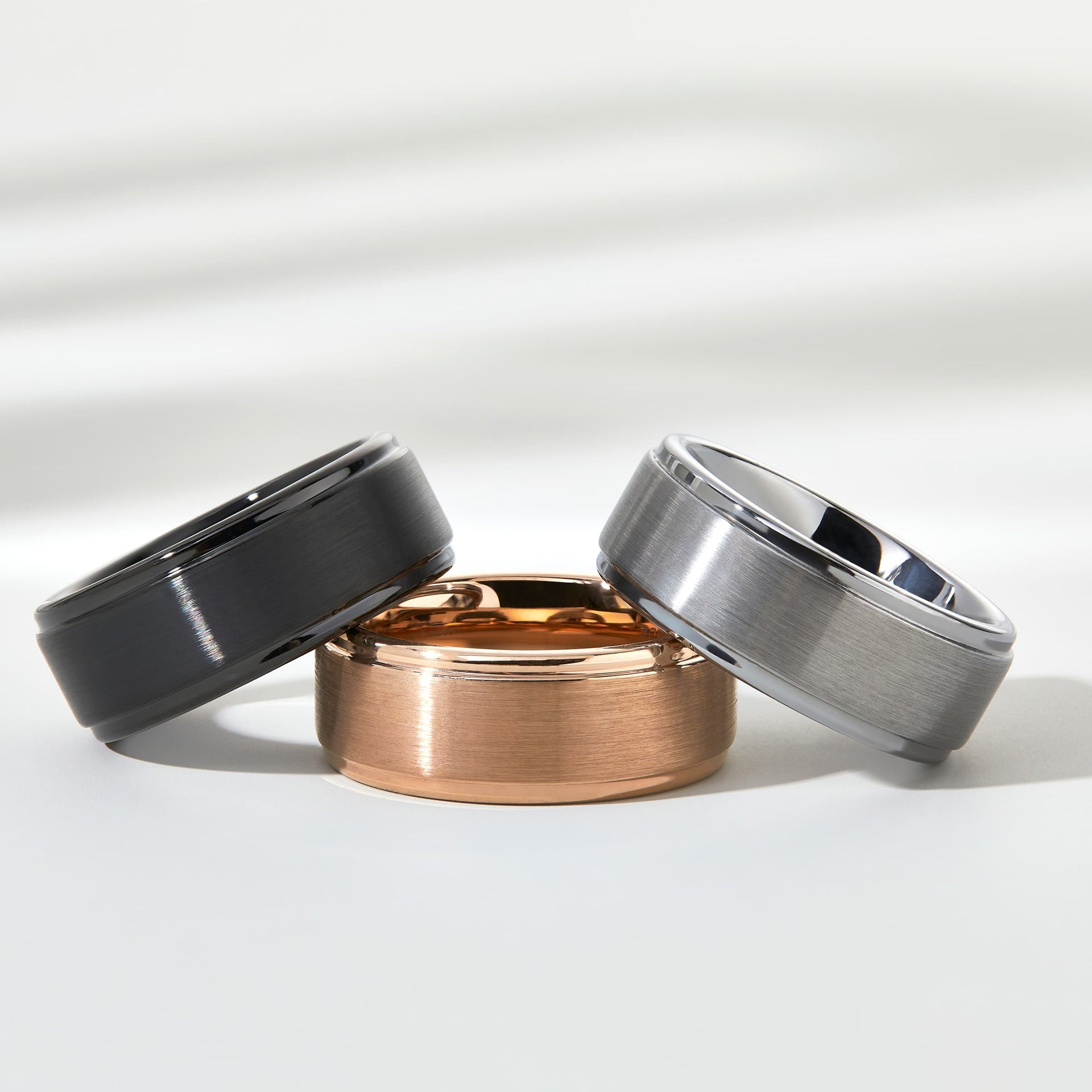 flatlay of black, rose gold, silver wedding band 