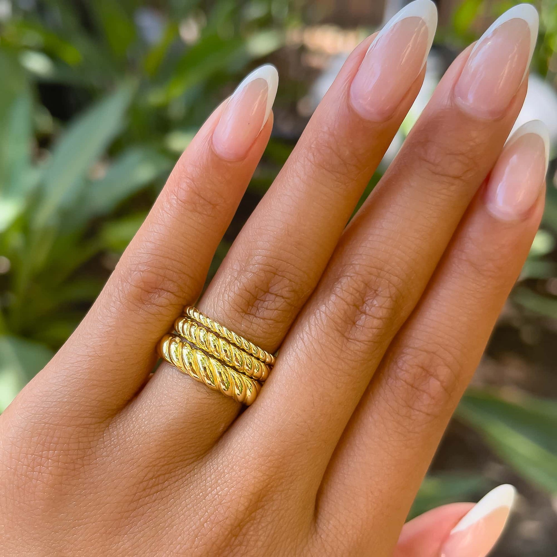 three beautiful gold rope wedding bands stacked on model's finger with french manicured nails and greenery in the background