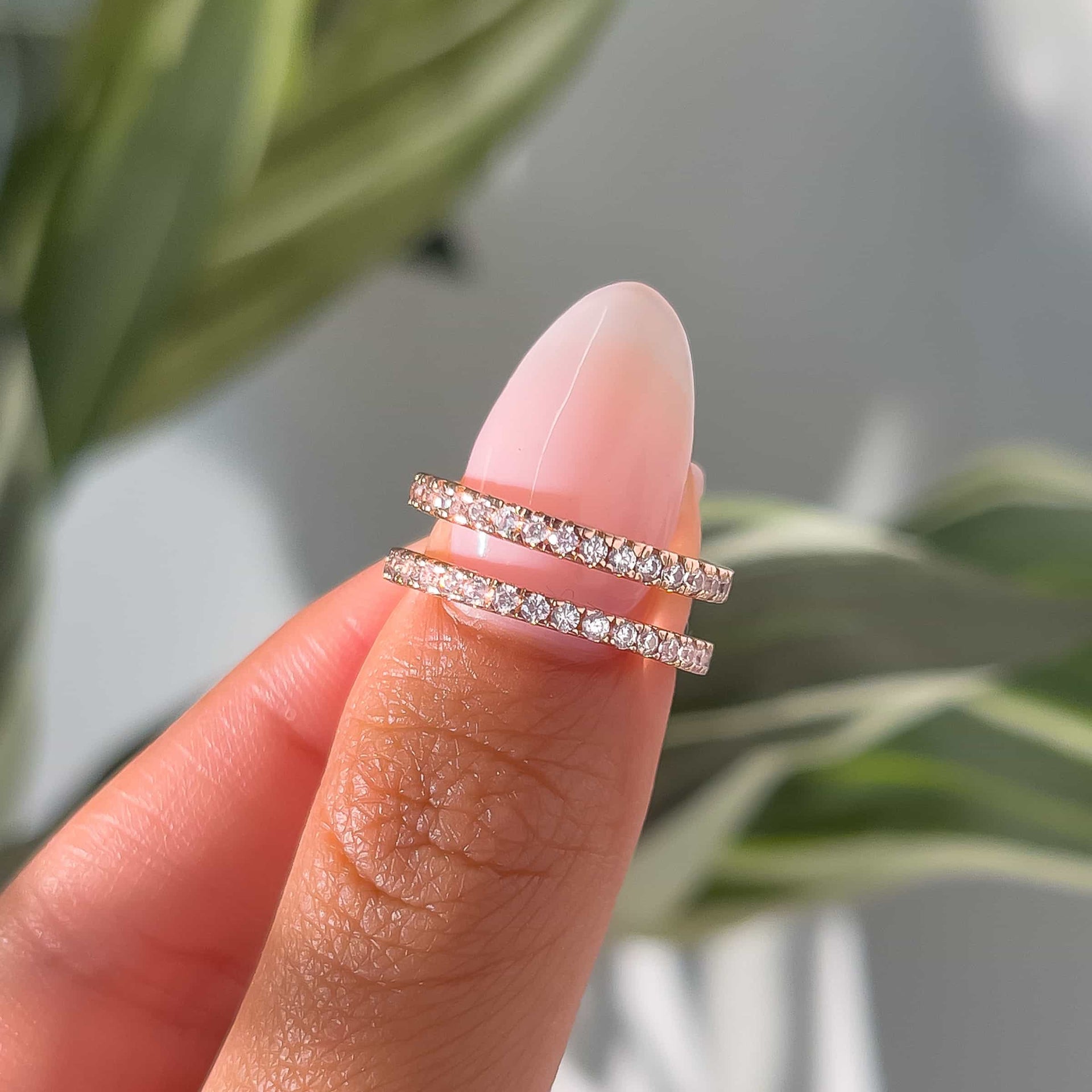 woman pinching two affordable rose gold wedding bands with green plant in background