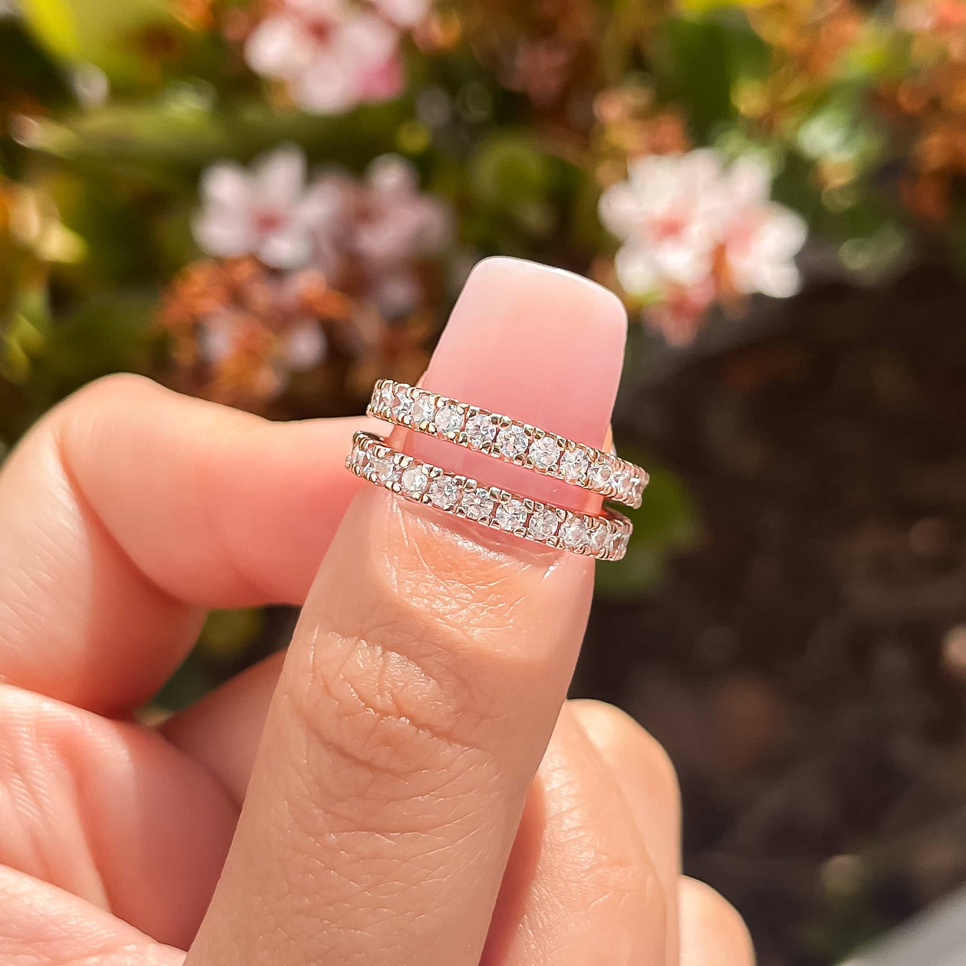 set of two rose gold eternity bands on thumb with neutral pink nail and greenery in the background