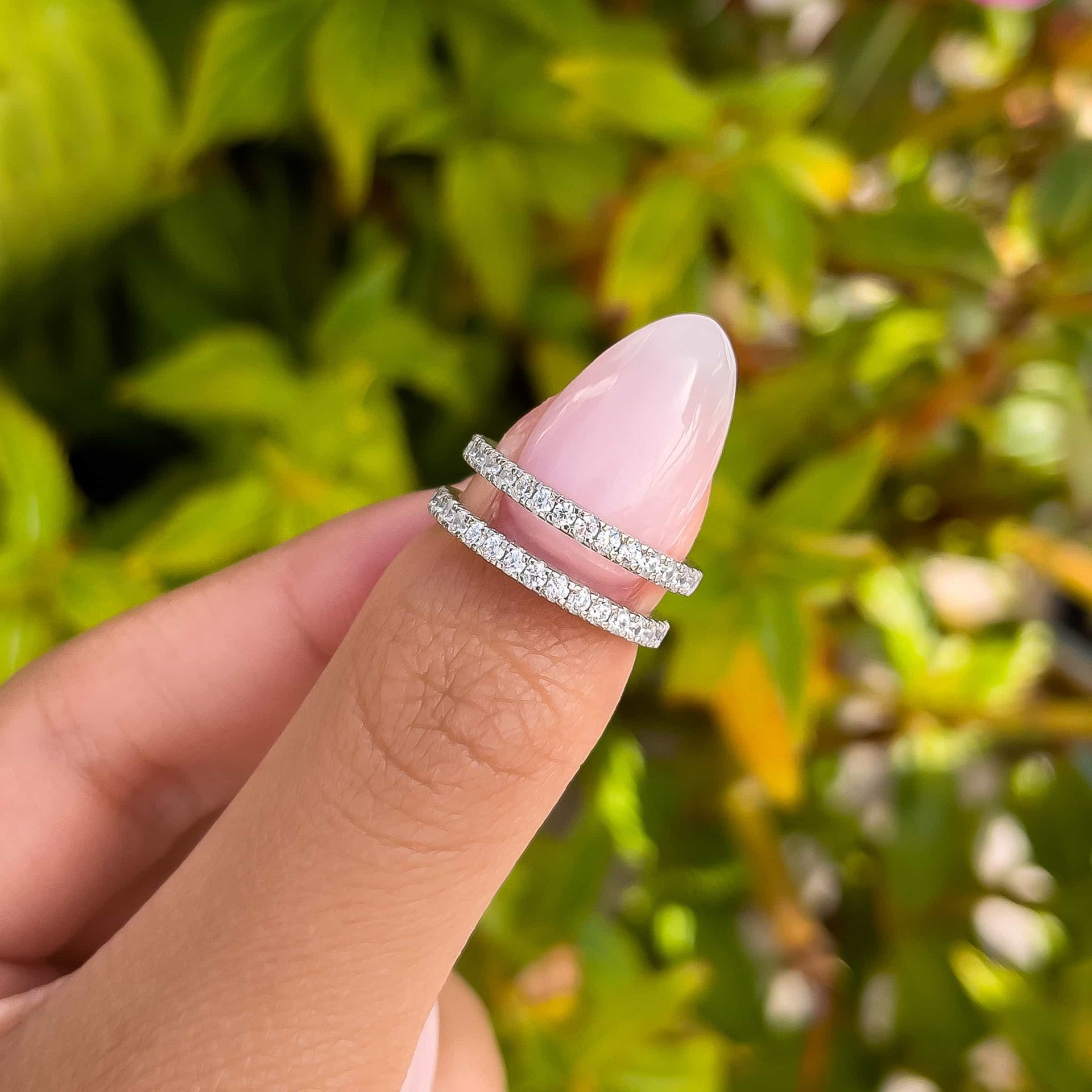 woman pinching two desire bands in silver with greenery in background