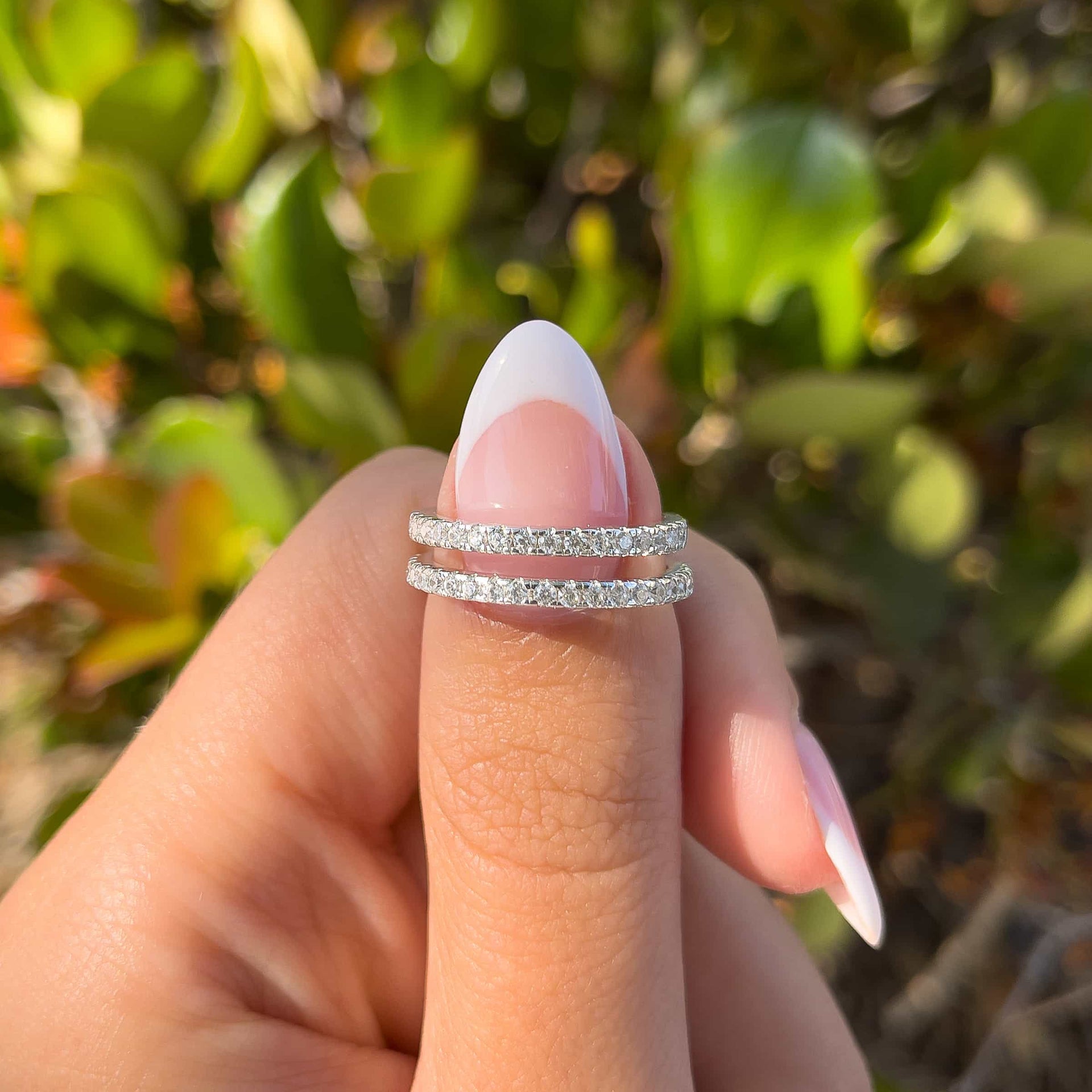 woman pinching two silver promise wedding bands with greenery in background