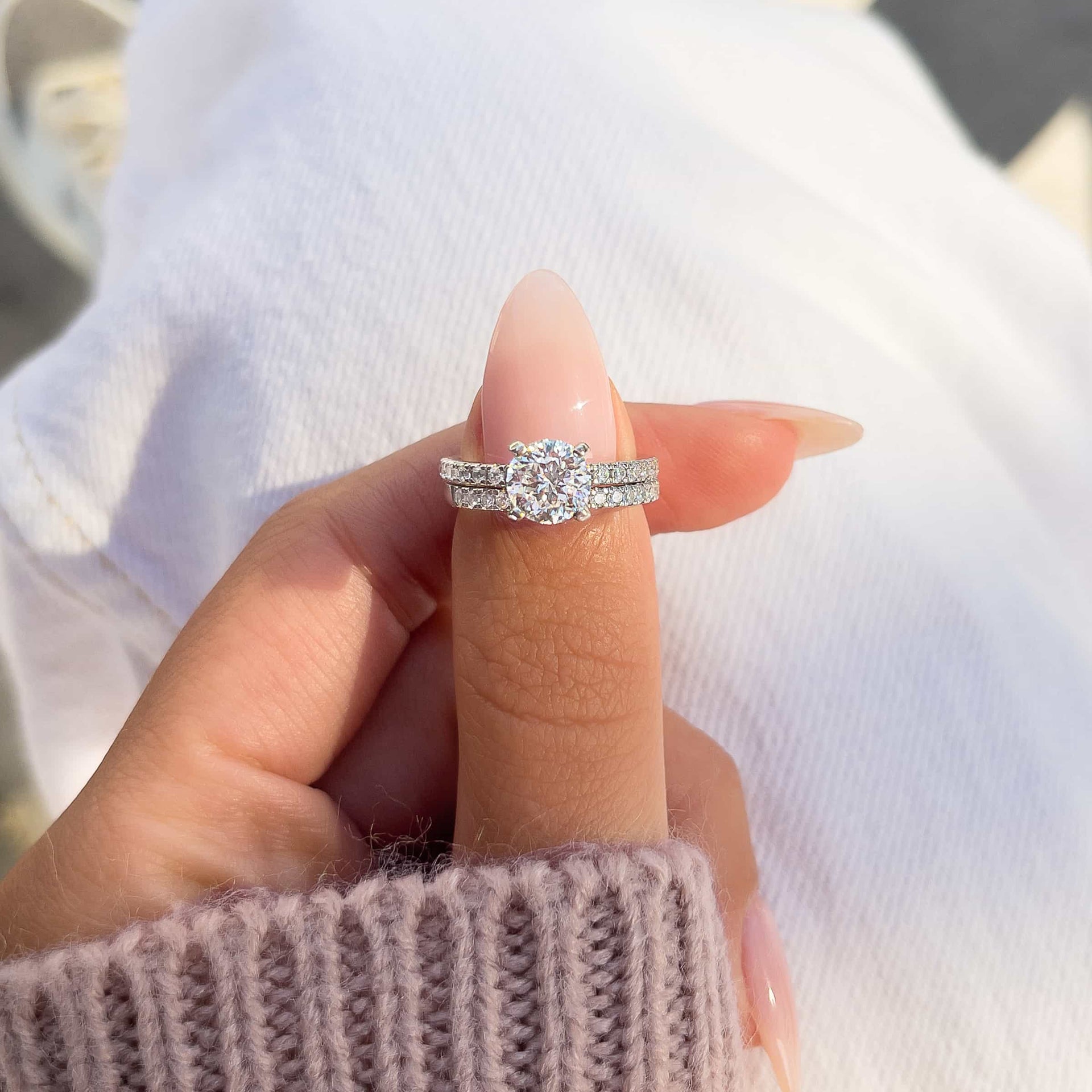 gorgeous round cut silver wedding ring set on woman's finger with purple sweater