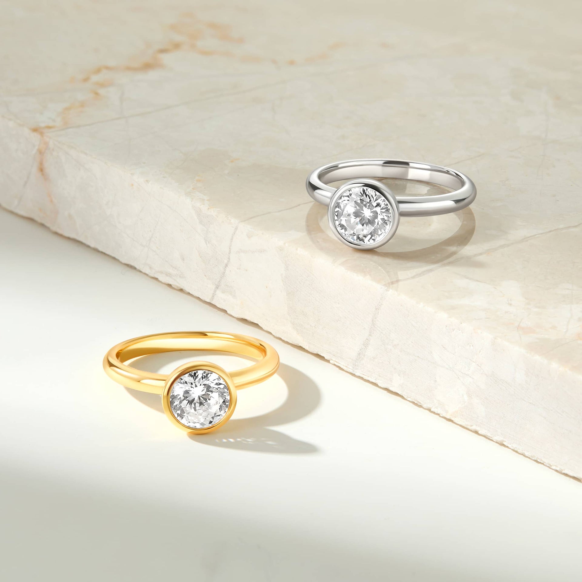 a stunning silver and gold round cut bezel engagement ring shown on a marbled background