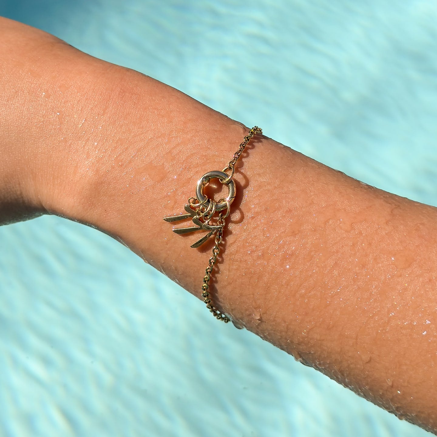 waterproof gold charm bracelet with three gold number charms "7", "7", & "7" worn on it by a model who is in the pool
