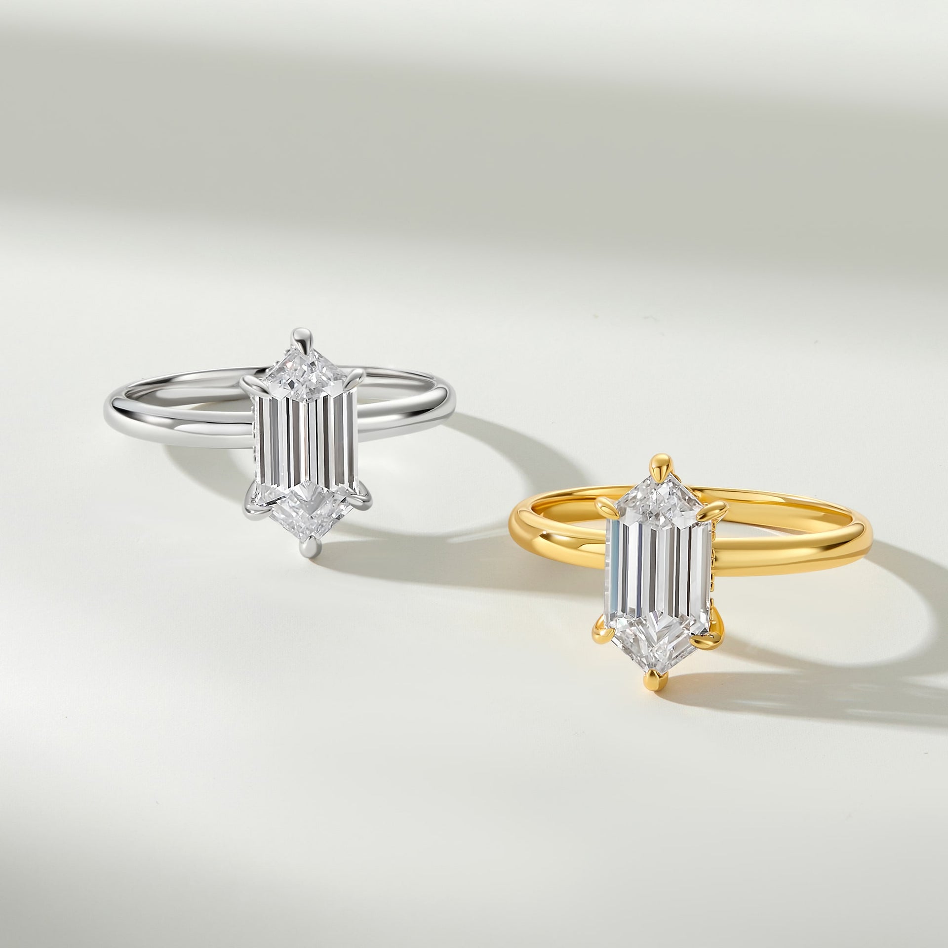 a 2.5 carat hexagon cut solitaire engagement ring shown in silver and gold, both sitting on an off white background