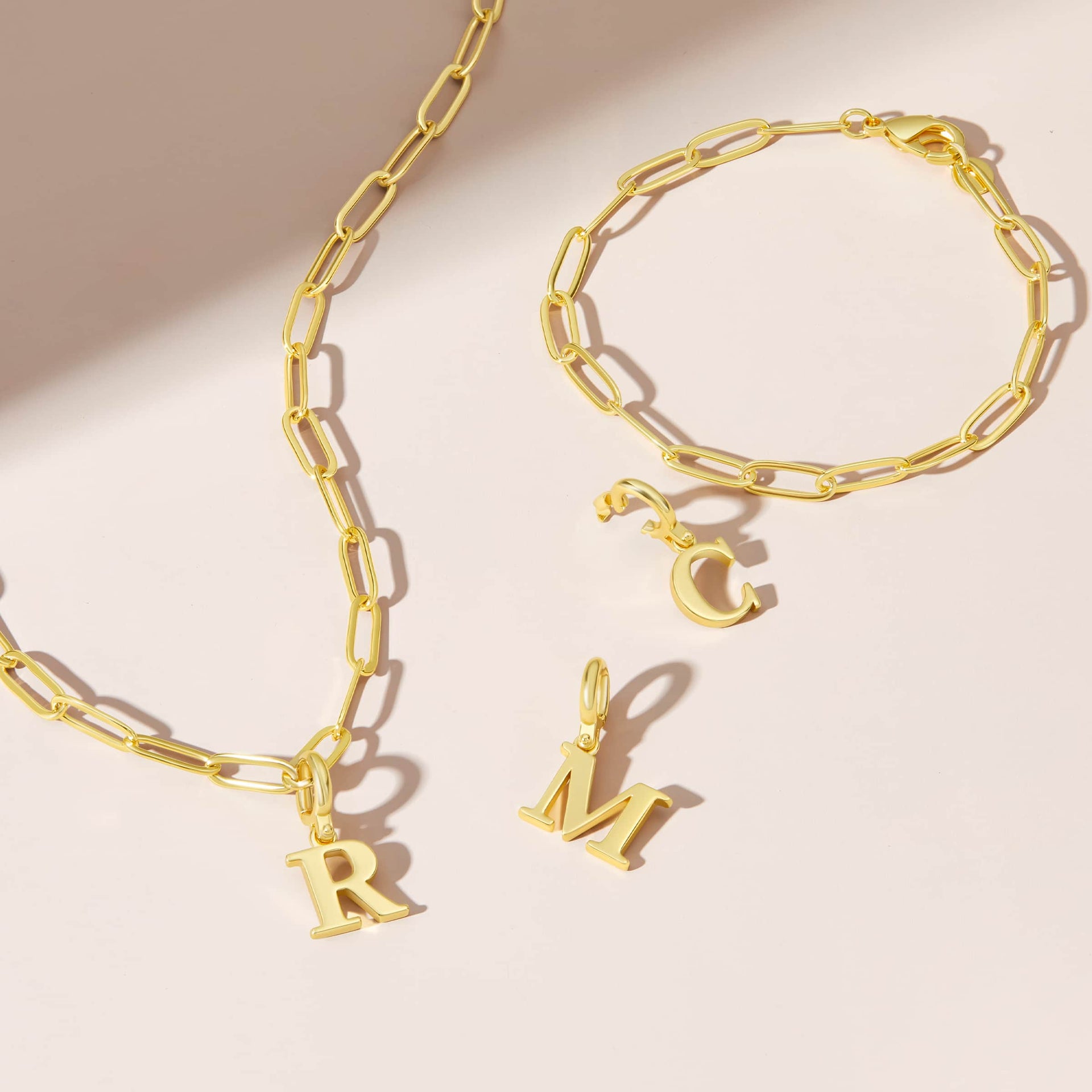 the gold letter charms shown in "R", "M", and "C" on both a necklace and bracelet