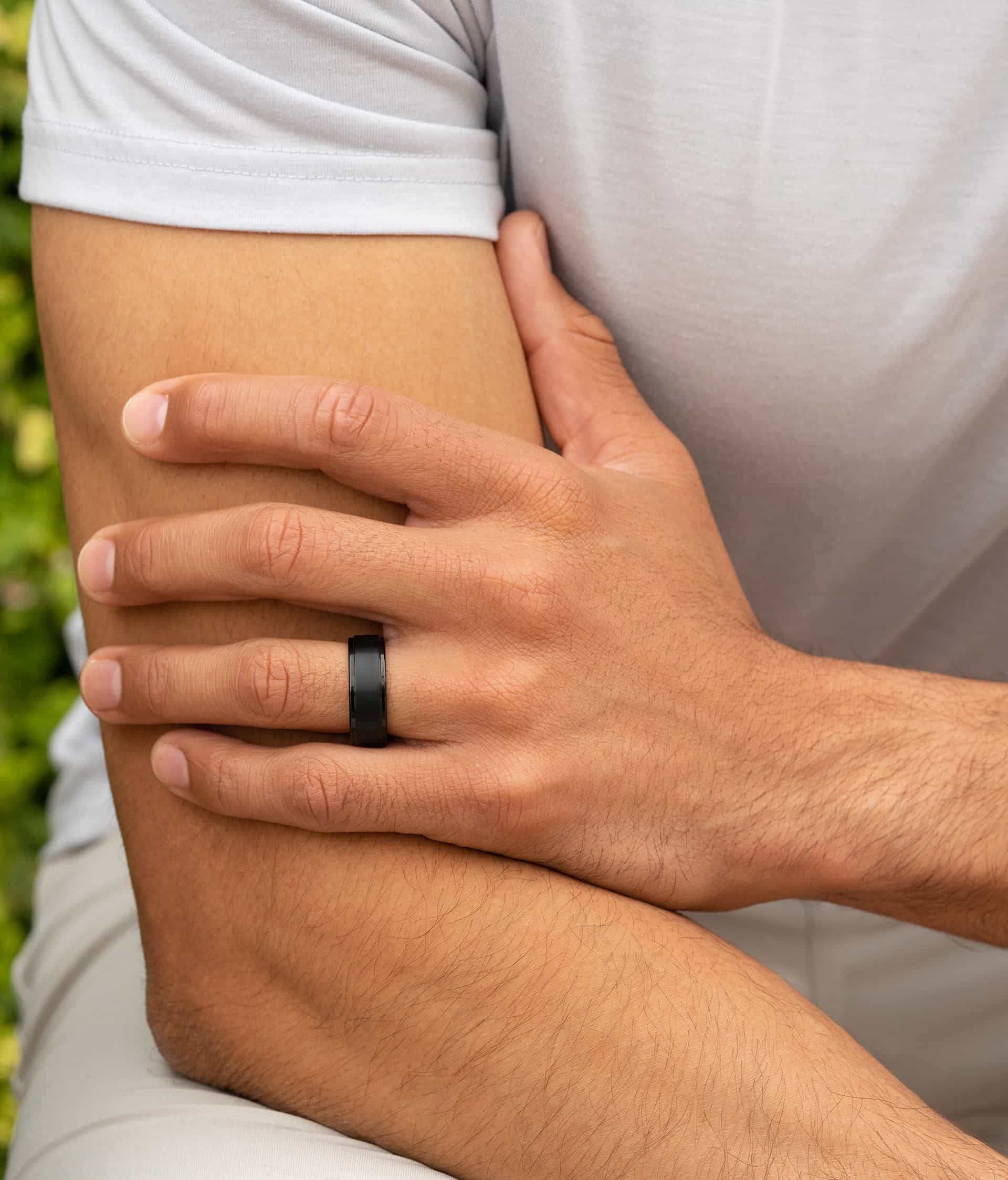 man wearing black wedding band with greenery in the background