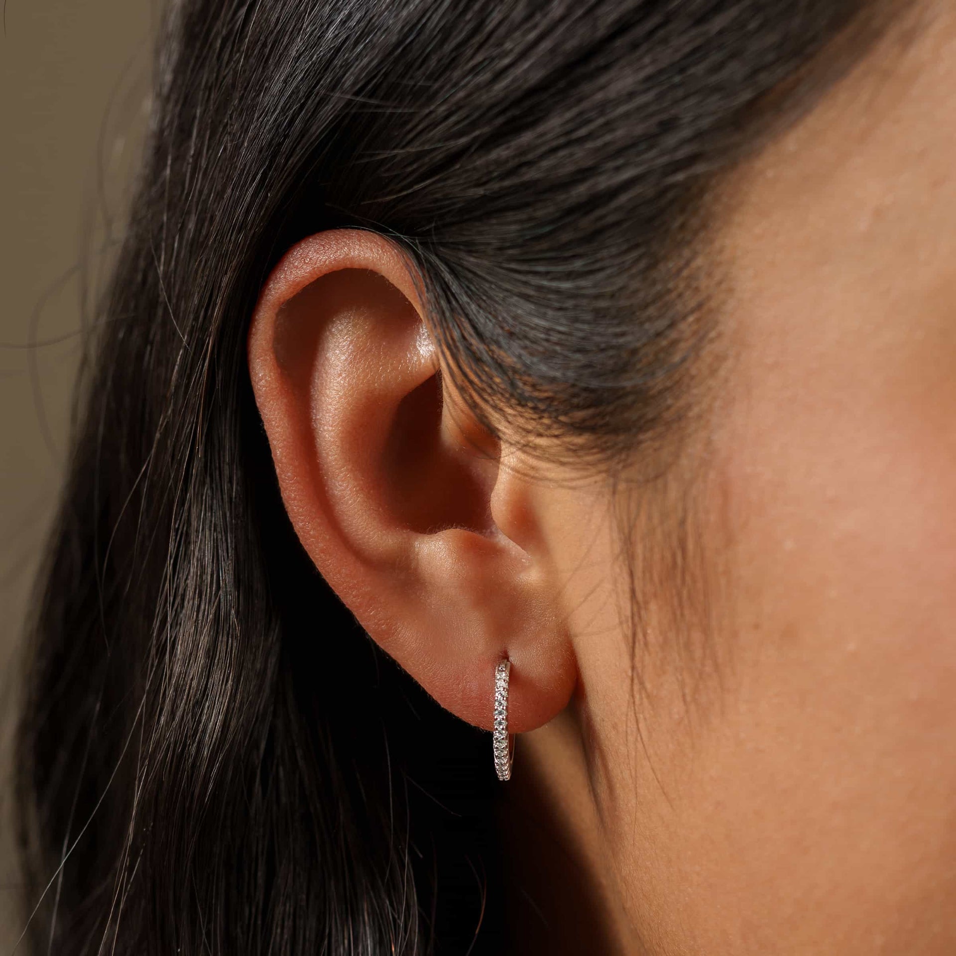 close up shot of simple dainty silver hoops adorned with stone detailing on a model