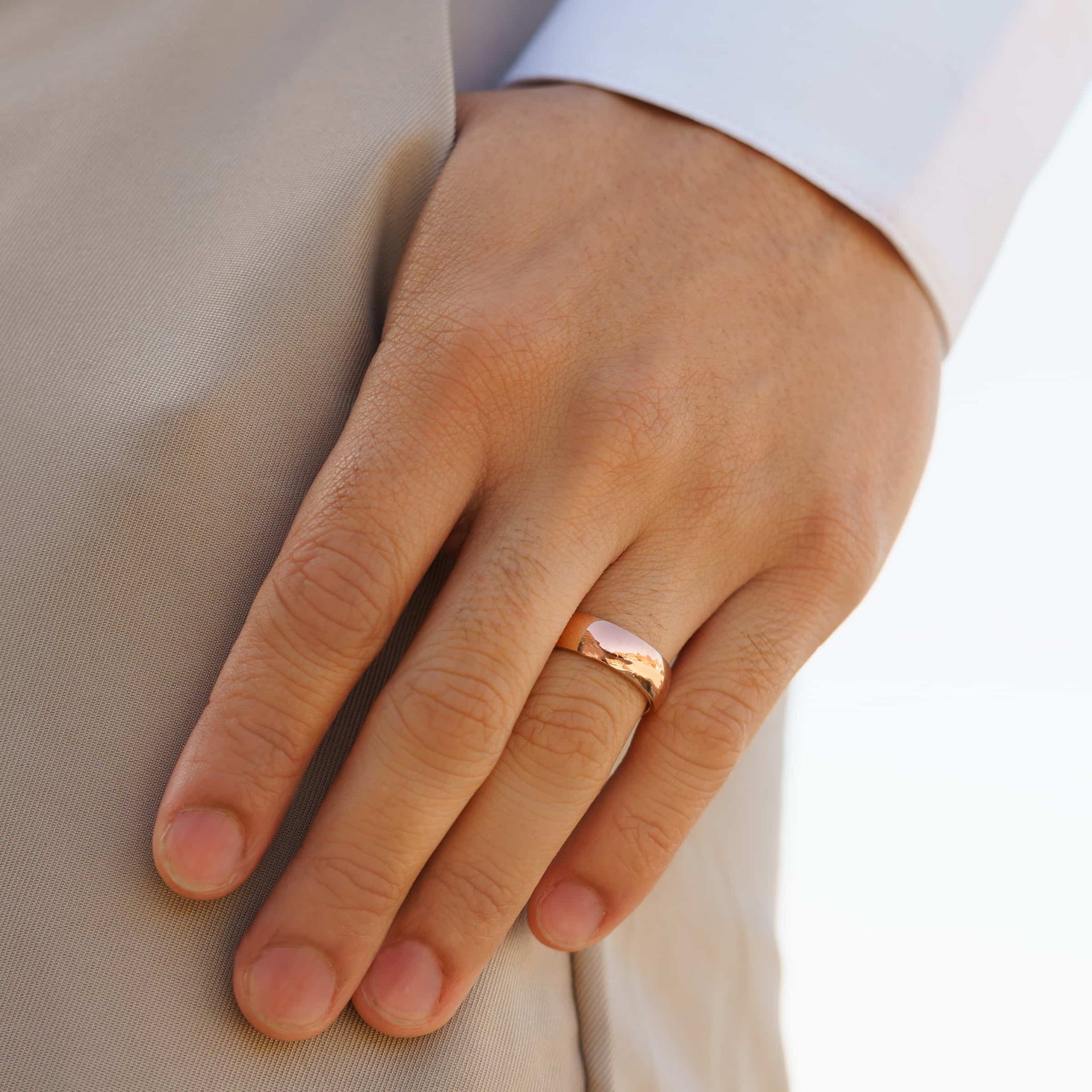stunning rose gold affordable unisex horizon wedding band on men's hand with white shirt and tan pants