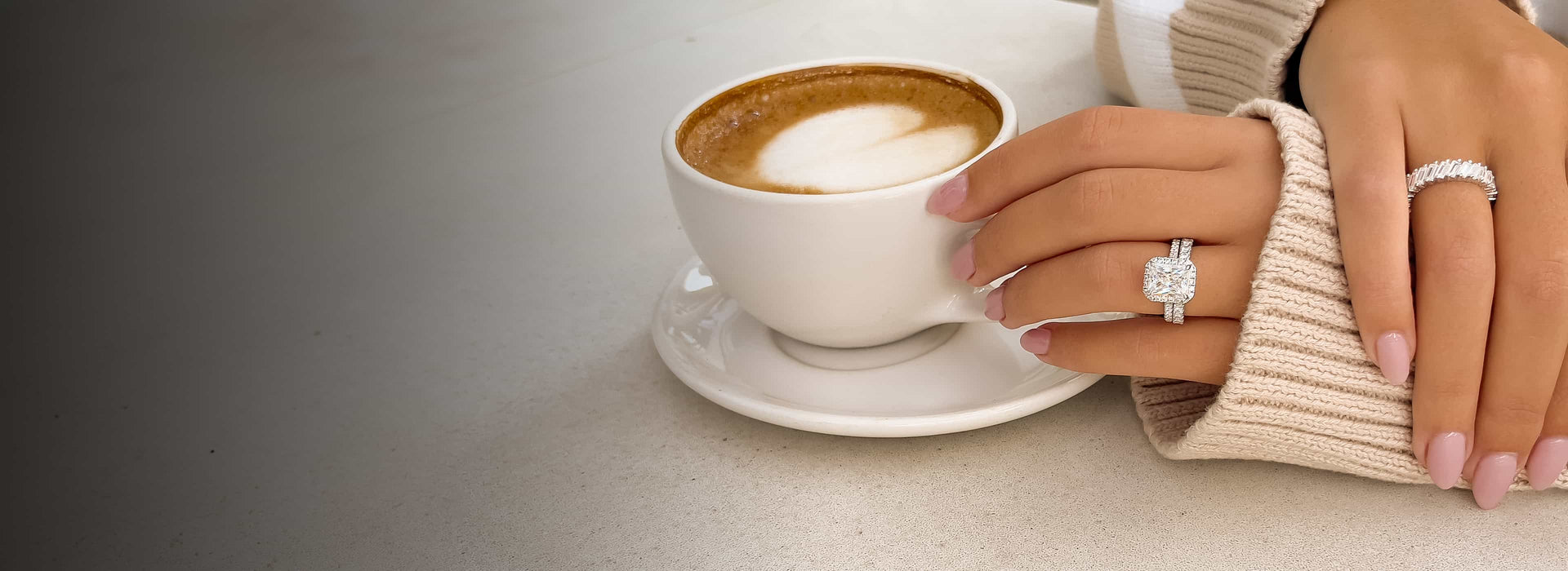 sparkling baguette wedding band and radiant cut wedding and engagement ring on hand of model with cream colored sweater holding a cup of coffee on a white table