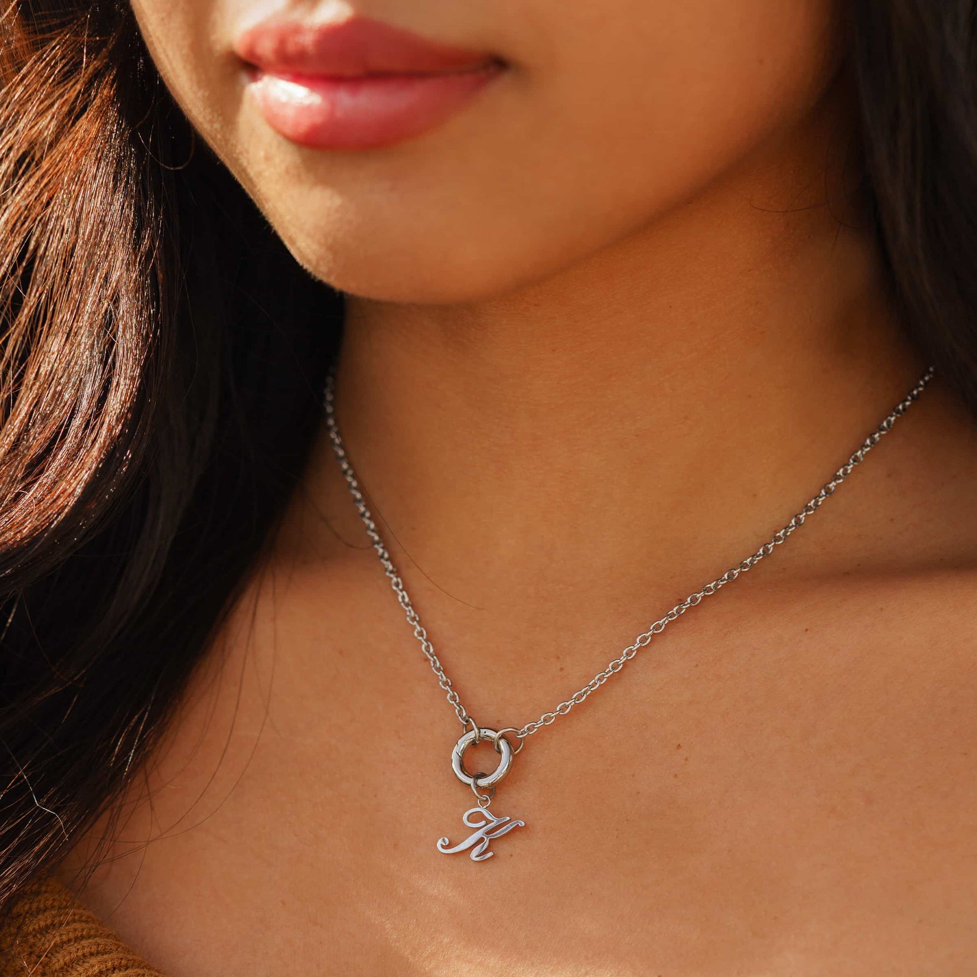 stainless steel letter charm "K" shown worn on a silver charm necklace worn by model with dark hair