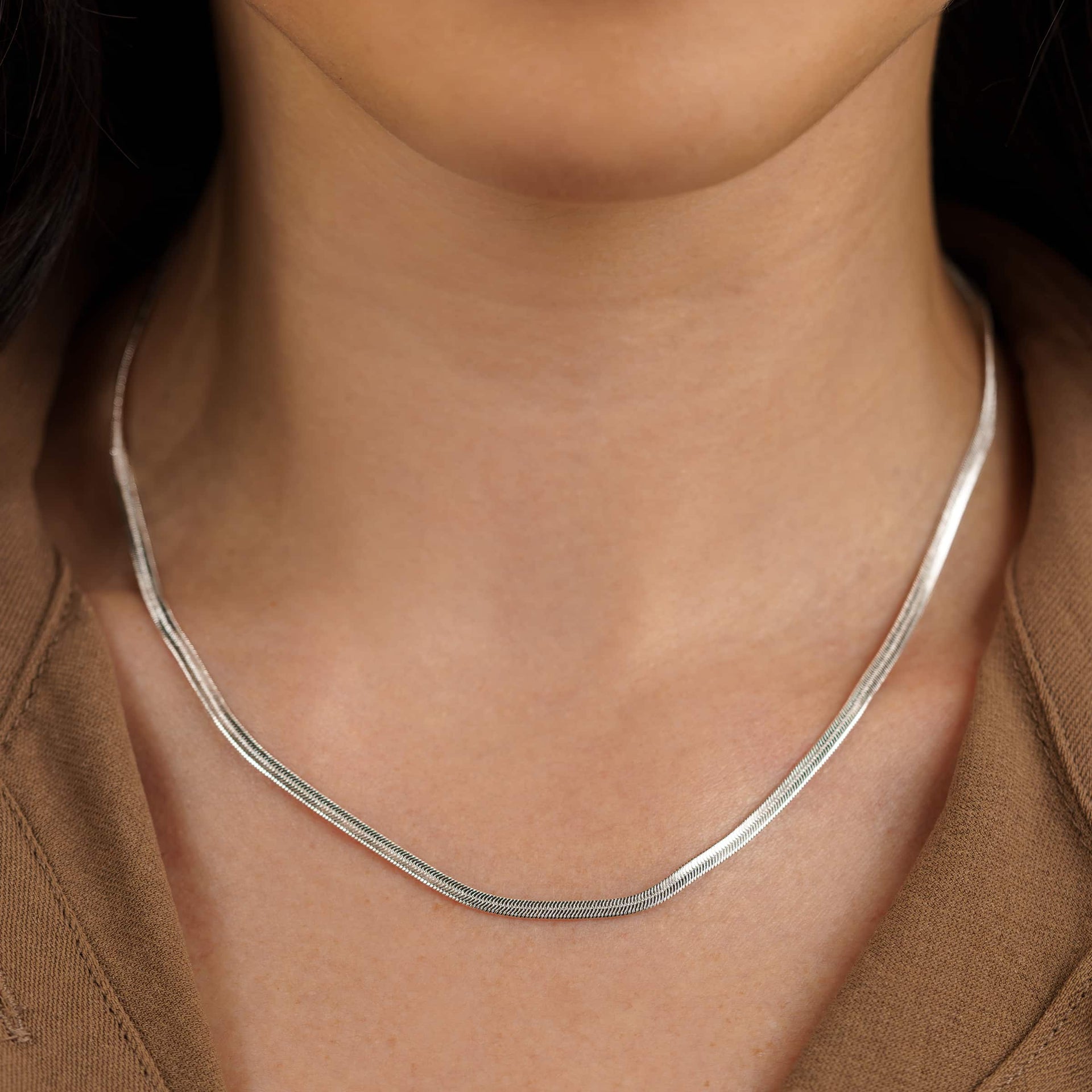 a slim, silver herringbone detail necklace on a model wearing a brown top